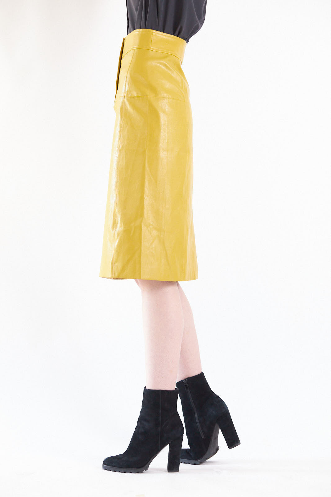 A person in a black star-patterned blazer, black turtleneck, Le Réussi® Power Woman- Mustard Leather Skirt, and black heeled boots poses against a plain background.