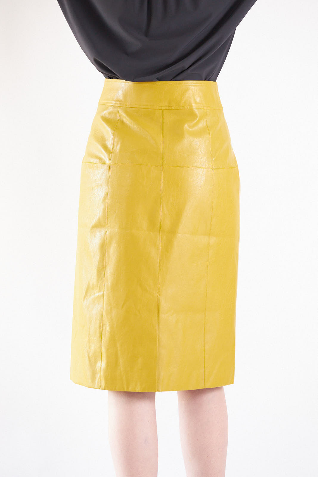 A person is wearing the Power Woman-Mustard Leather Skirt by Le Réussi® and black heeled ankle boots, standing against a white background.