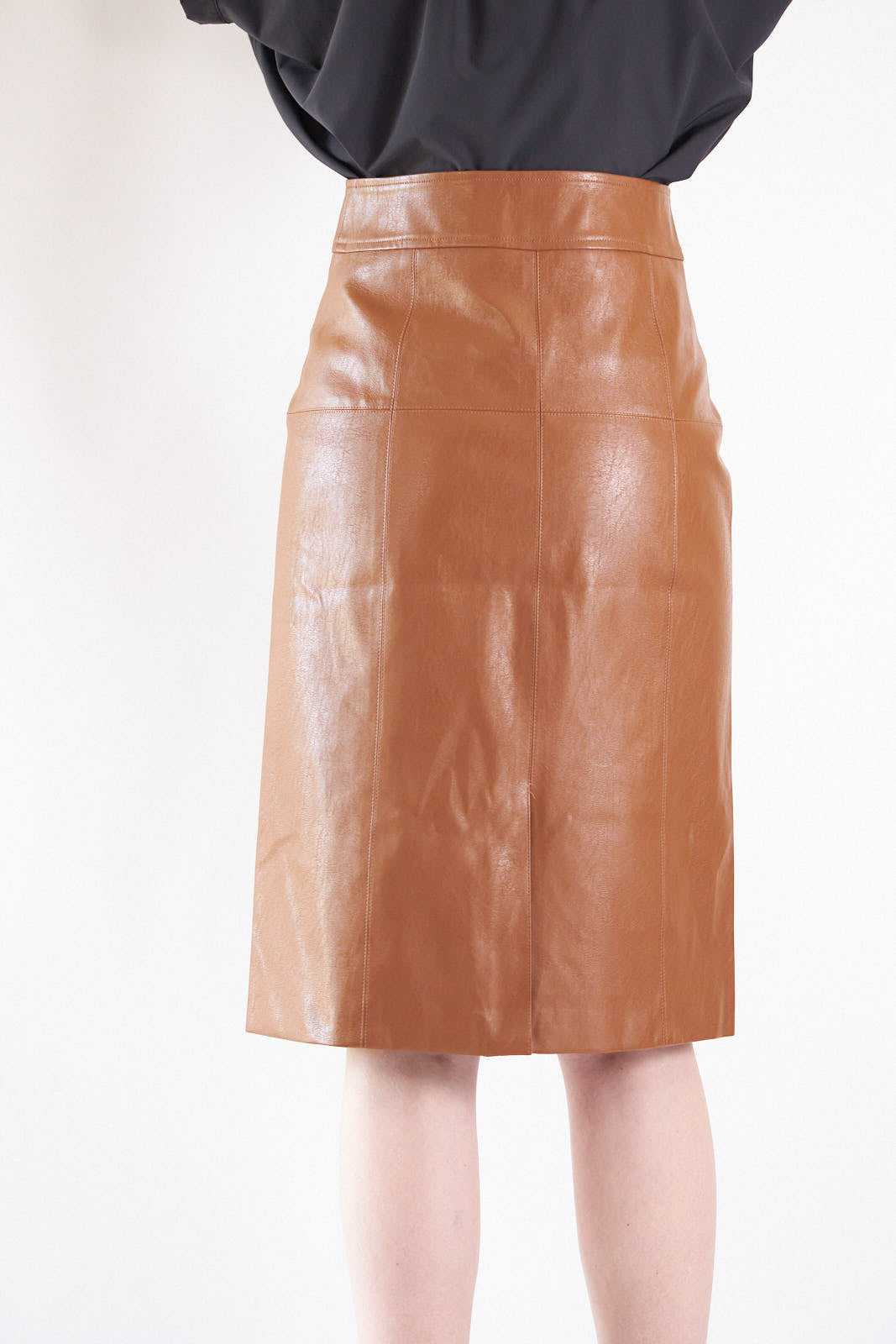 A person wearing a black top, Le Réussi® Power Woman- Dark Hazel Leather Skirt, and black high-heeled boots poses against a plain background.