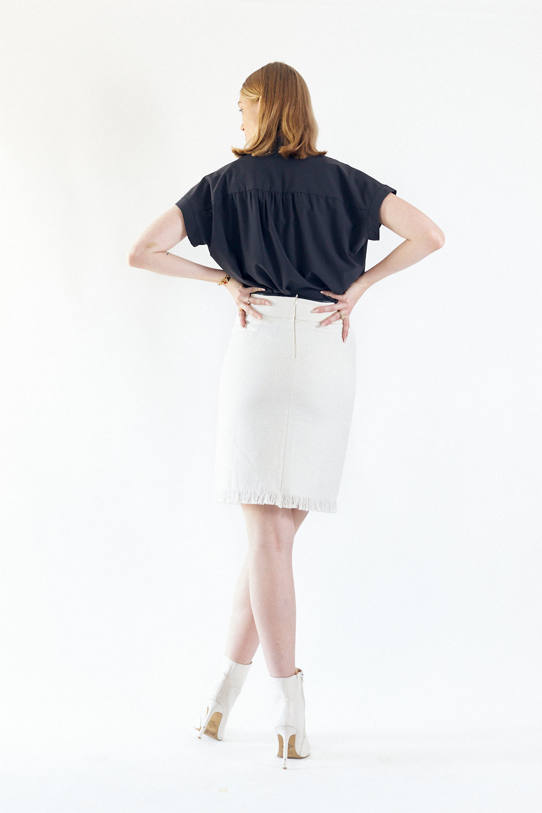 A side view of a person with red hair wearing a black top, Le Réussi®s Power Woman- White Tweed Skirt, and white boots, posing against a plain background.