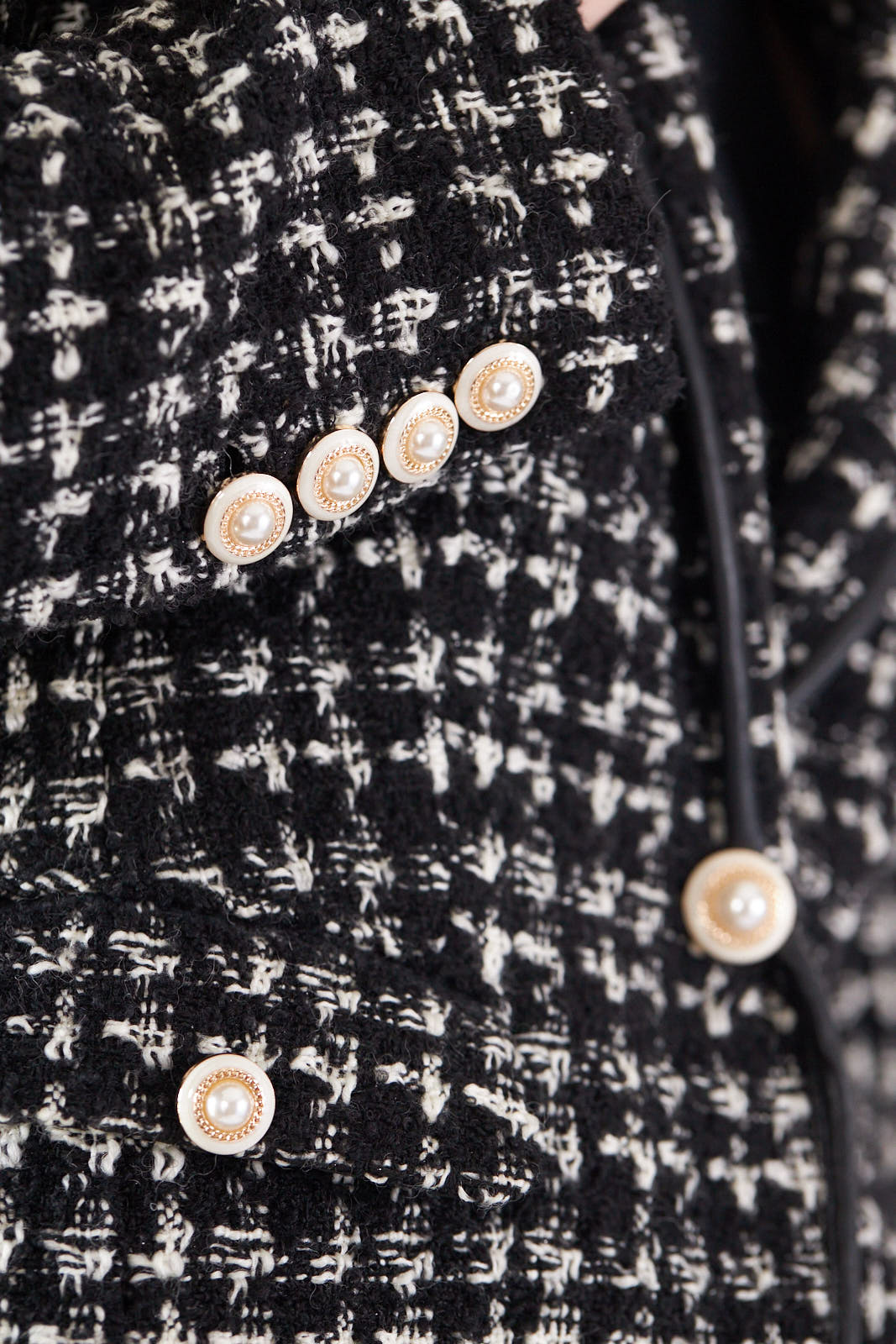 A person poses against a plain backdrop, wearing the Le Réussi® Power Woman- Black & White Tweed Checkers Jacket over a black shirt and white skirt.