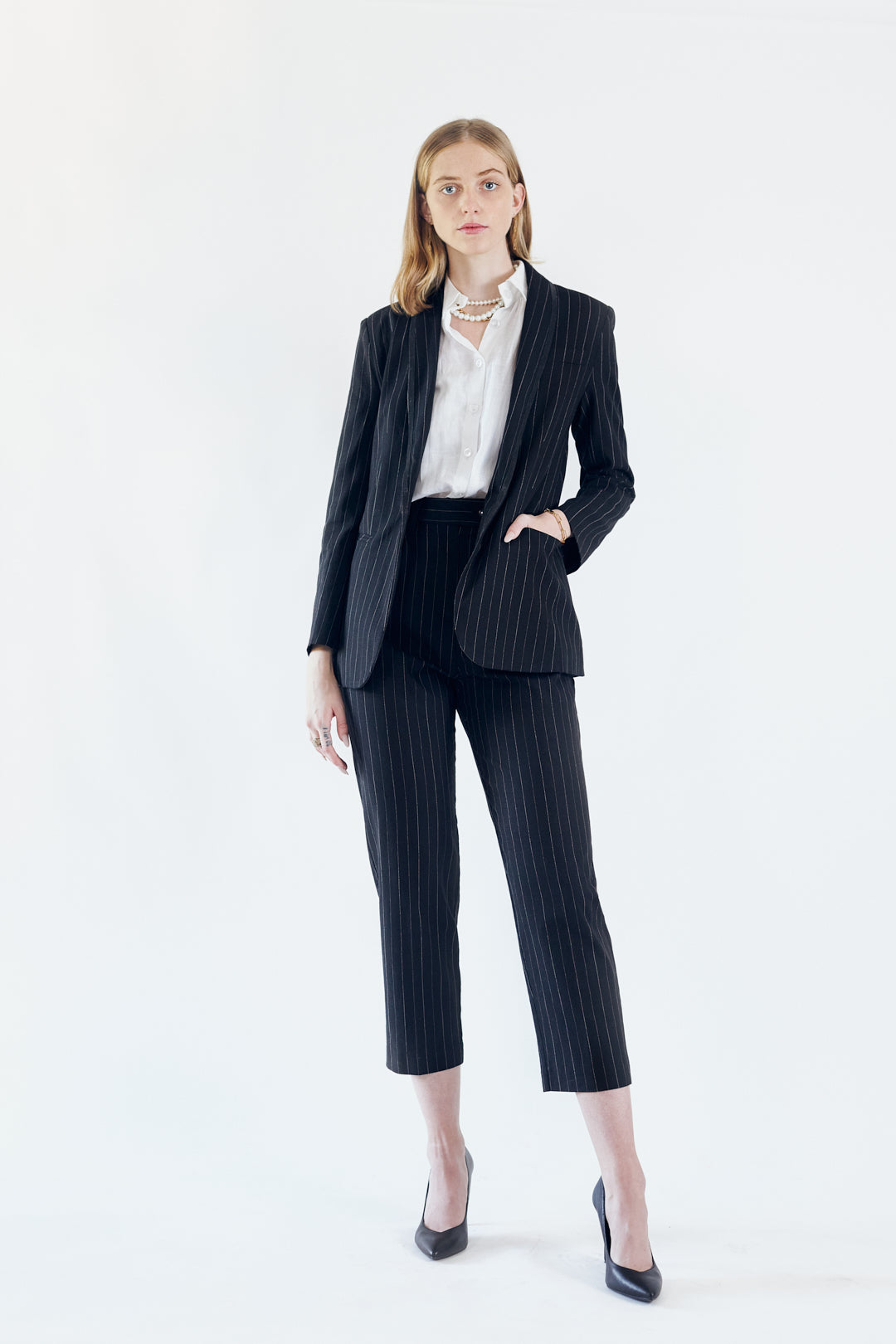 A person wearing the Le Réussi® Power Woman- Black/White Stripes Jacket with a white shirt stands stylishly with one hand in their pocket.