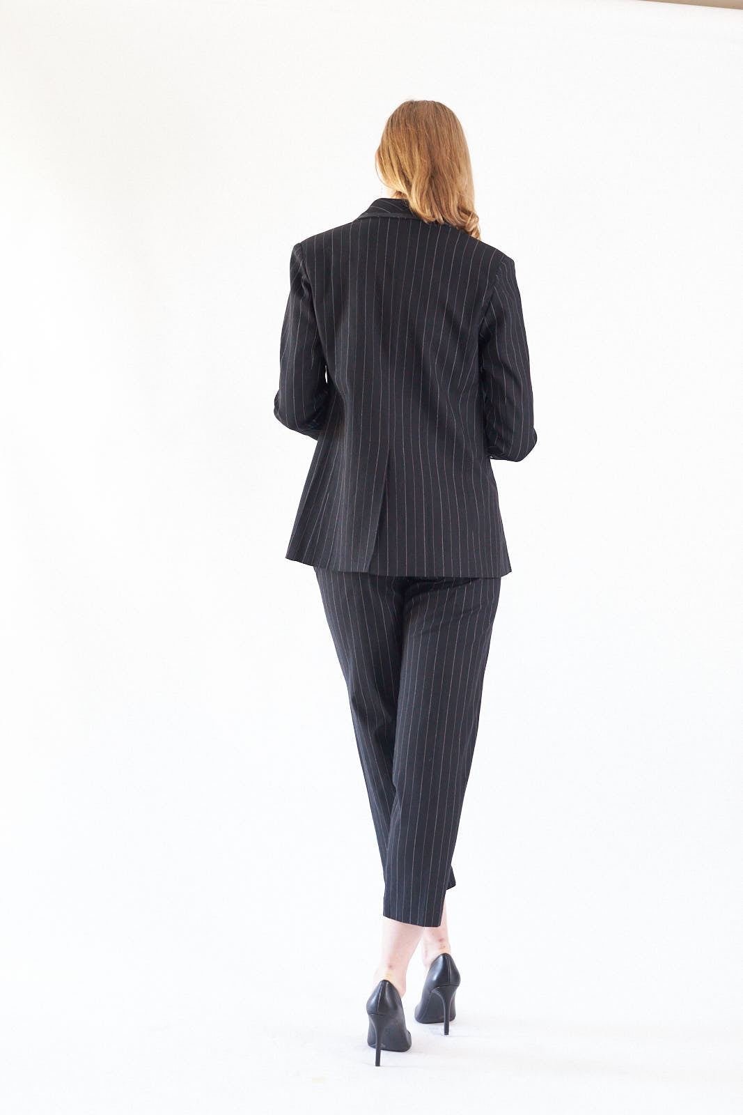 A person wearing the Le Réussi® Power Woman- Black/White Stripes Jacket with a white shirt stands stylishly with one hand in their pocket.