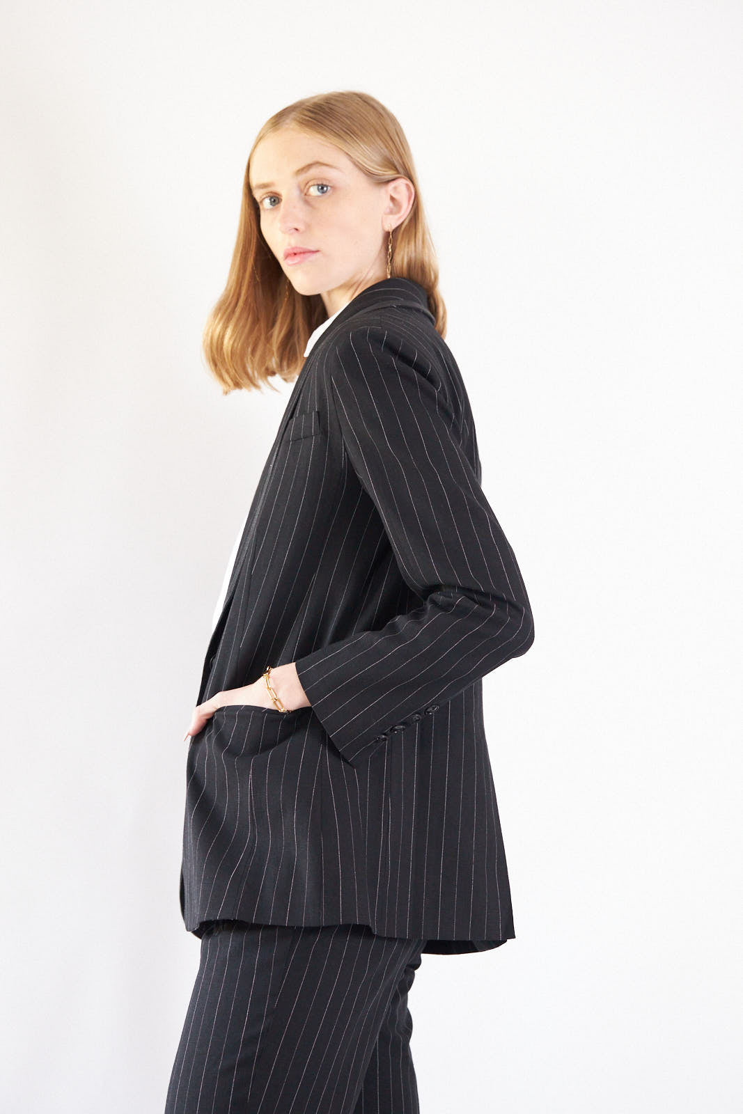 A person wearing the Le Réussi® Power Woman- Black/White Stripes Jacket with a white shirt stands stylishly with one hand in their pocket.