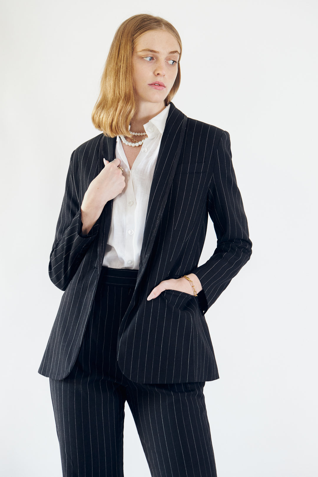 A person wearing the Le Réussi® Power Woman- Black/White Stripes Jacket with a white shirt stands stylishly with one hand in their pocket.
