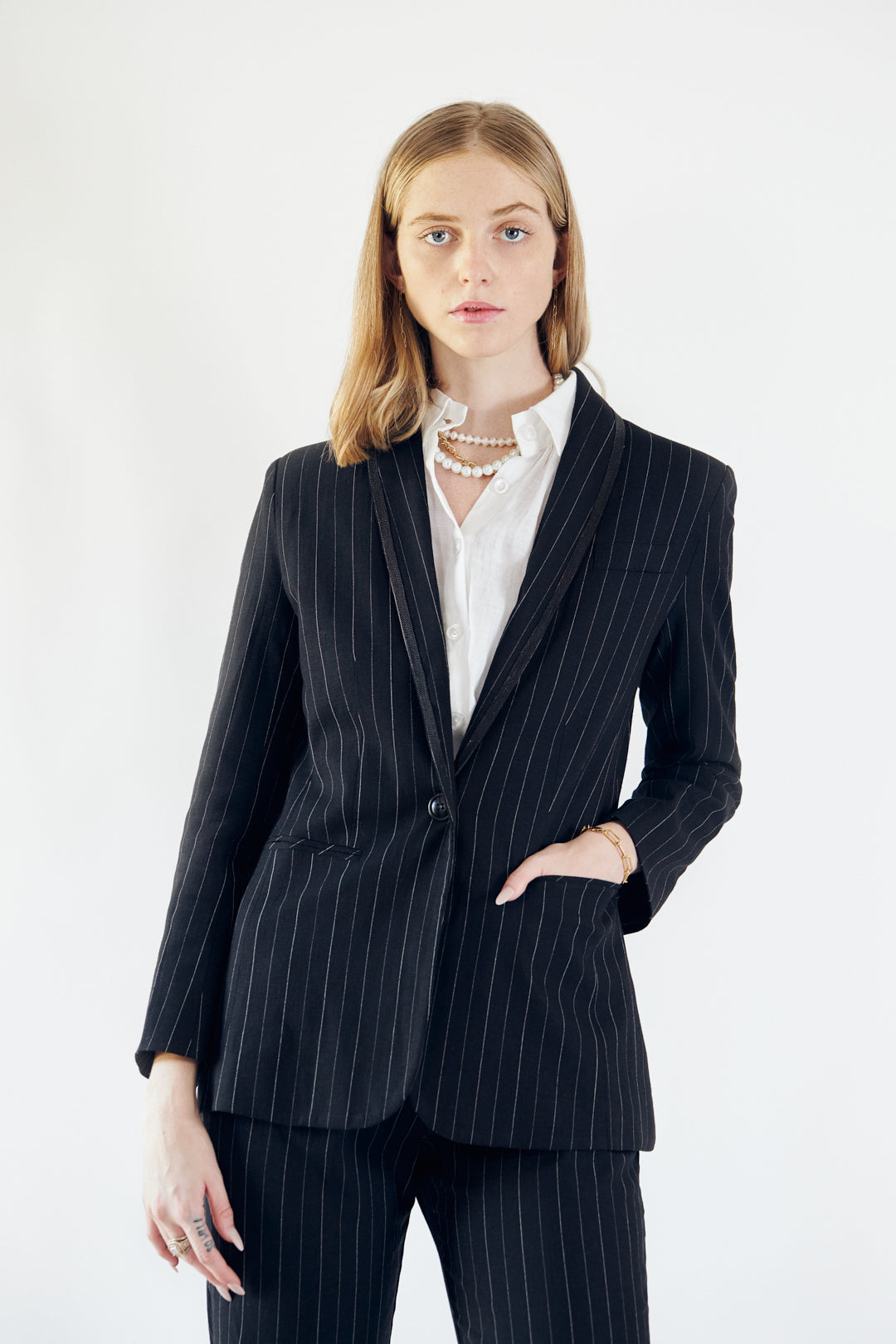A person wearing the Le Réussi® Power Woman- Black/White Stripes Jacket with a white shirt stands stylishly with one hand in their pocket.