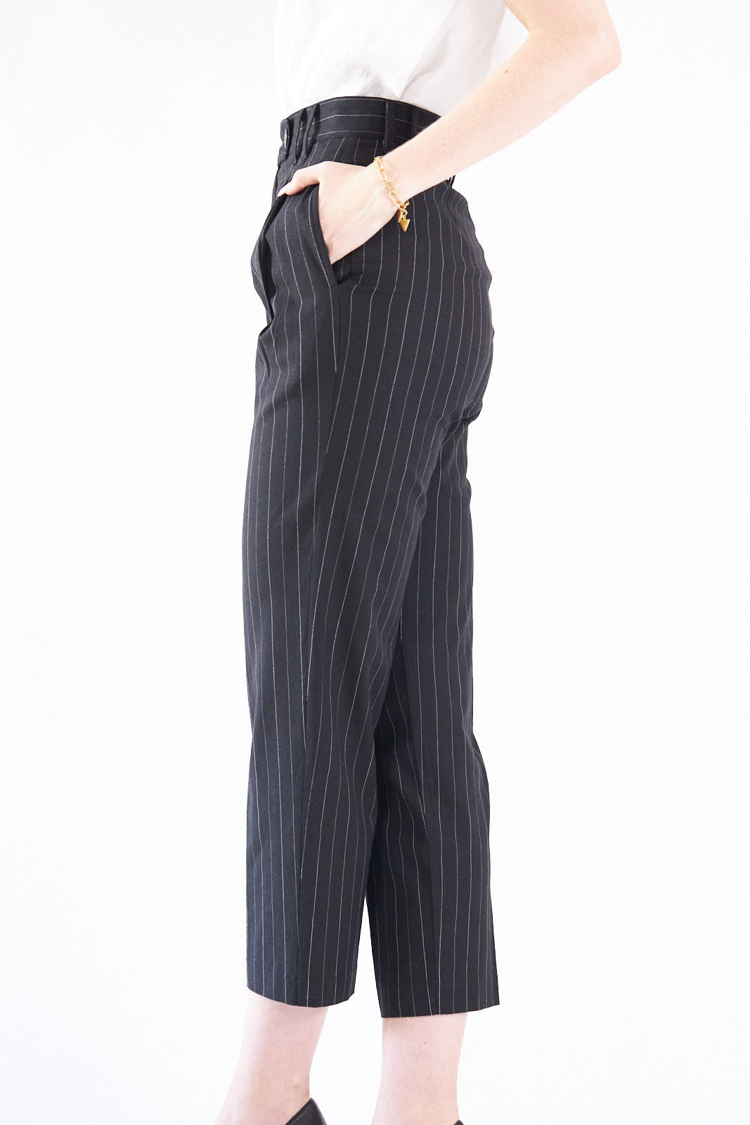 A woman exudes confidence in Le Réussi®s Power Woman- Black/White Stripes Pants paired with a white blouse, standing stylishly with one hand in her pocket against a white background.
