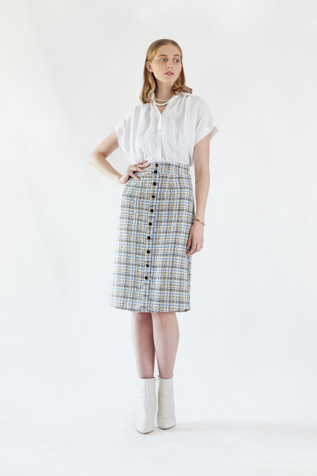 A person is wearing the Power Woman- Eye Catching Tweed Skirt by Le Réussi®, a high-waisted, button-down plaid skirt in blue, beige, and white, paired with a white blouse.