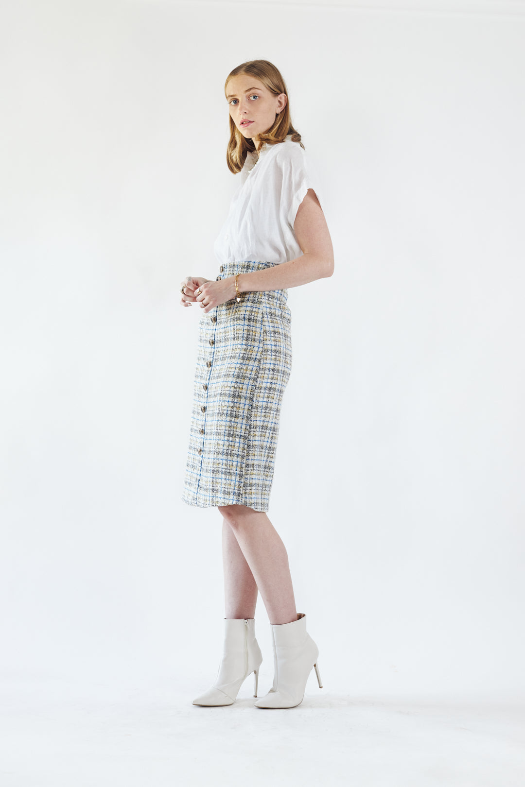 A person is wearing the Power Woman- Eye Catching Tweed Skirt by Le Réussi®, a high-waisted, button-down plaid skirt in blue, beige, and white, paired with a white blouse.