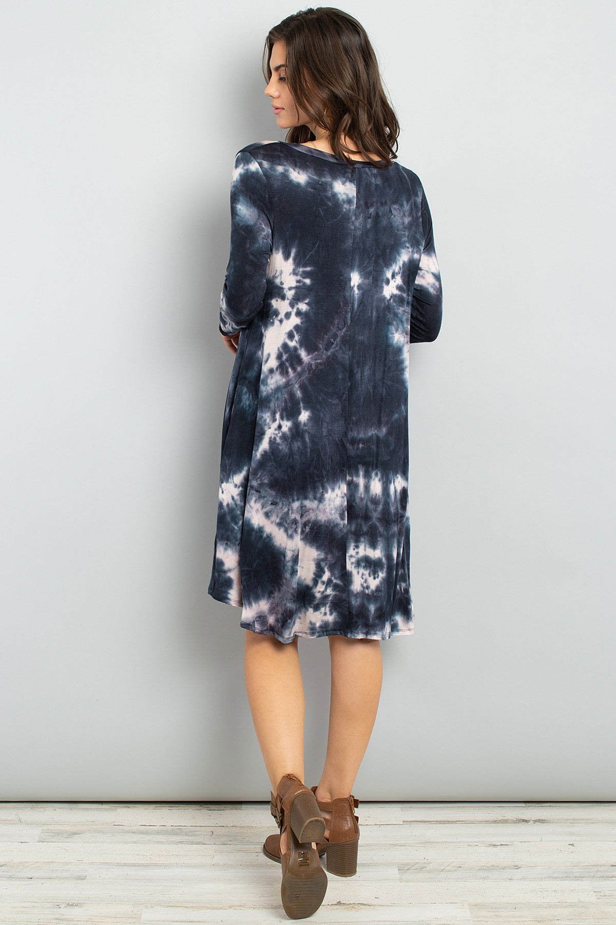 A woman in a purple Tie Dye V-Neck Rounded Hem Midi Dress by Riah Fashion, touching her hair, stands against a beige background.