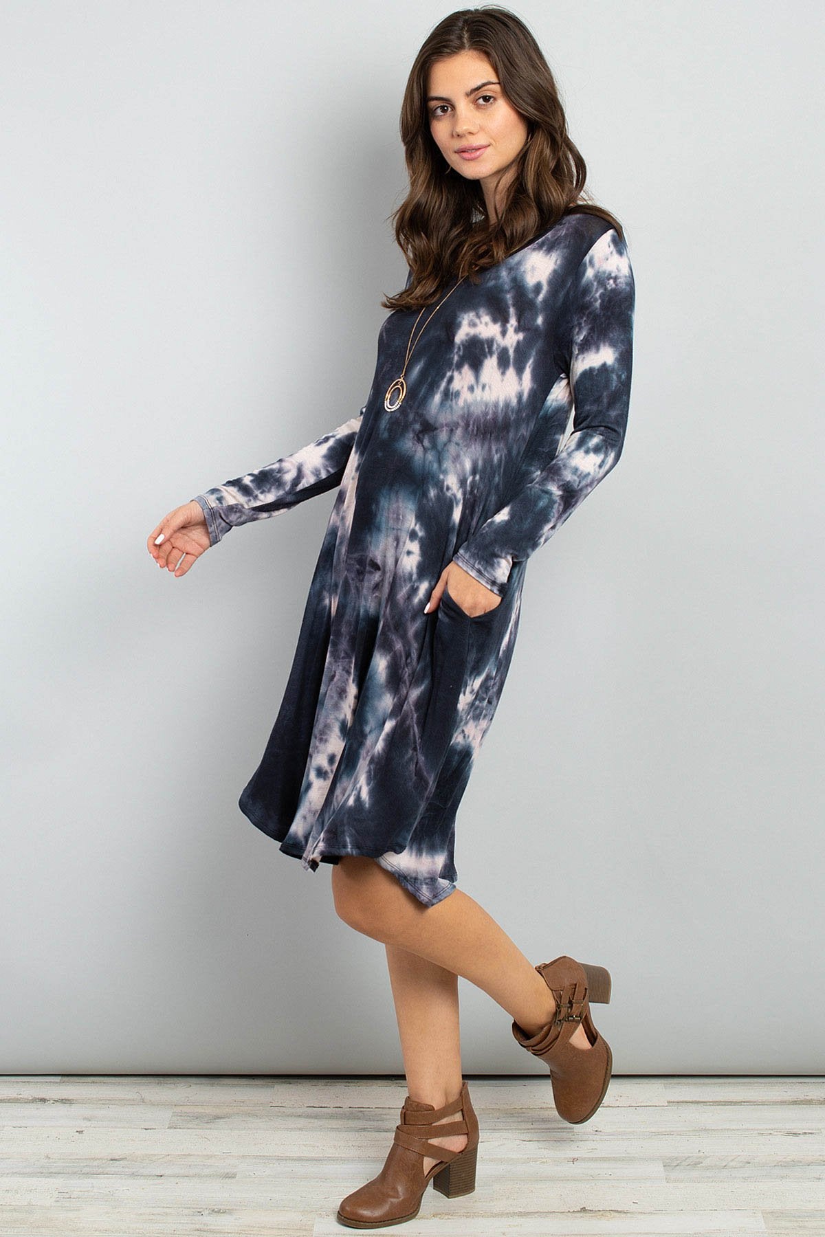 A woman in a purple Tie Dye V-Neck Rounded Hem Midi Dress by Riah Fashion, touching her hair, stands against a beige background.