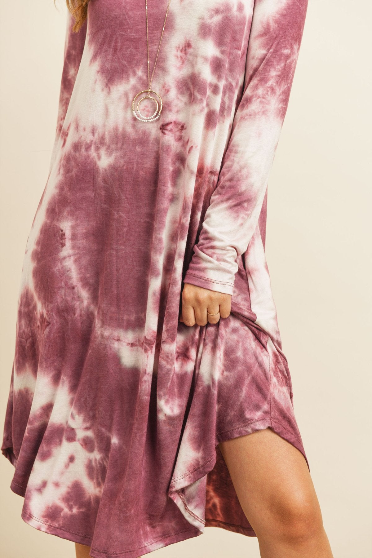A woman in a purple Tie Dye V-Neck Rounded Hem Midi Dress by Riah Fashion, touching her hair, stands against a beige background.