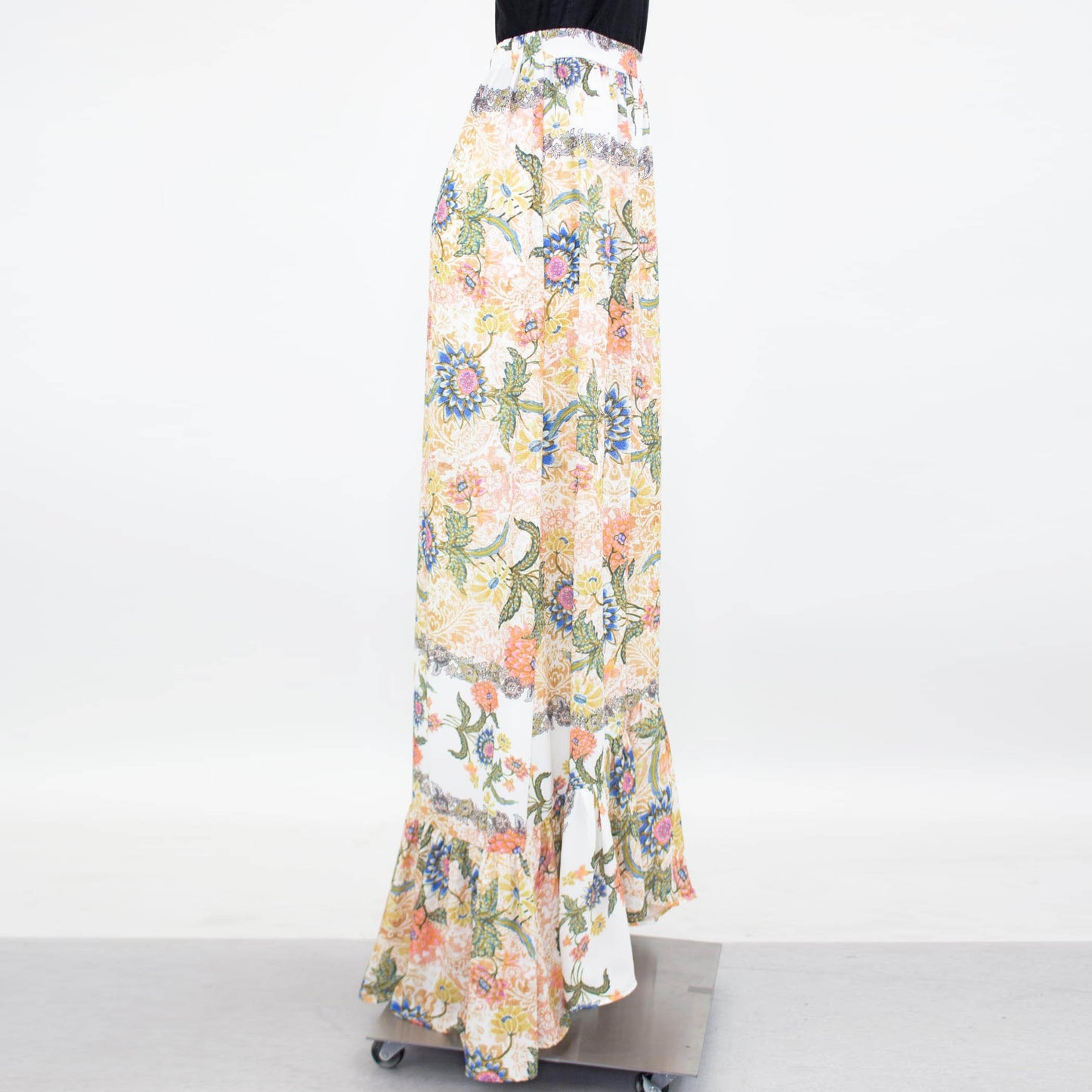 Stylespects Flared Bottom Floral Maxi Skirt showcases a ruffled hem with an array of orange, pink, blue, and green patterns set against a white background.