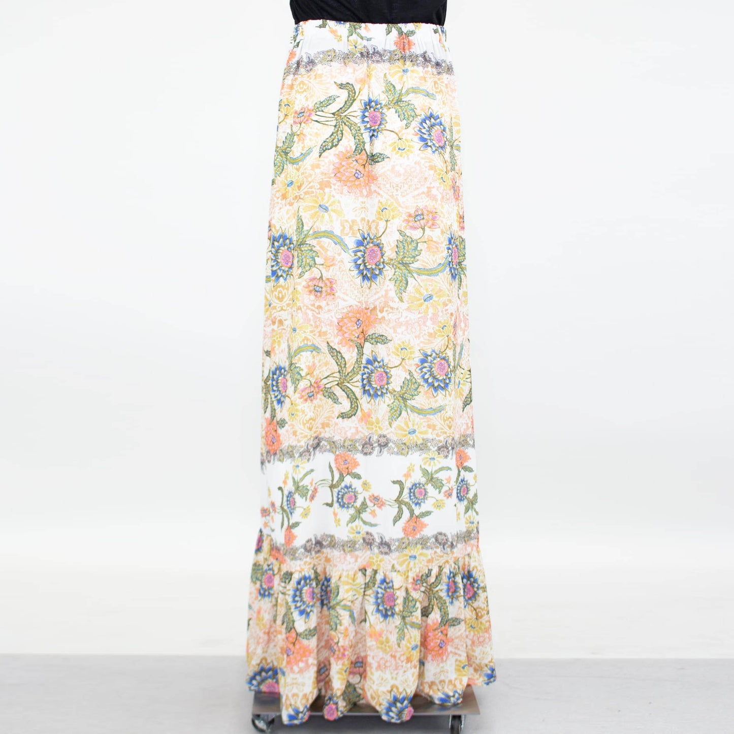 Stylespects Flared Bottom Floral Maxi Skirt showcases a ruffled hem with an array of orange, pink, blue, and green patterns set against a white background.