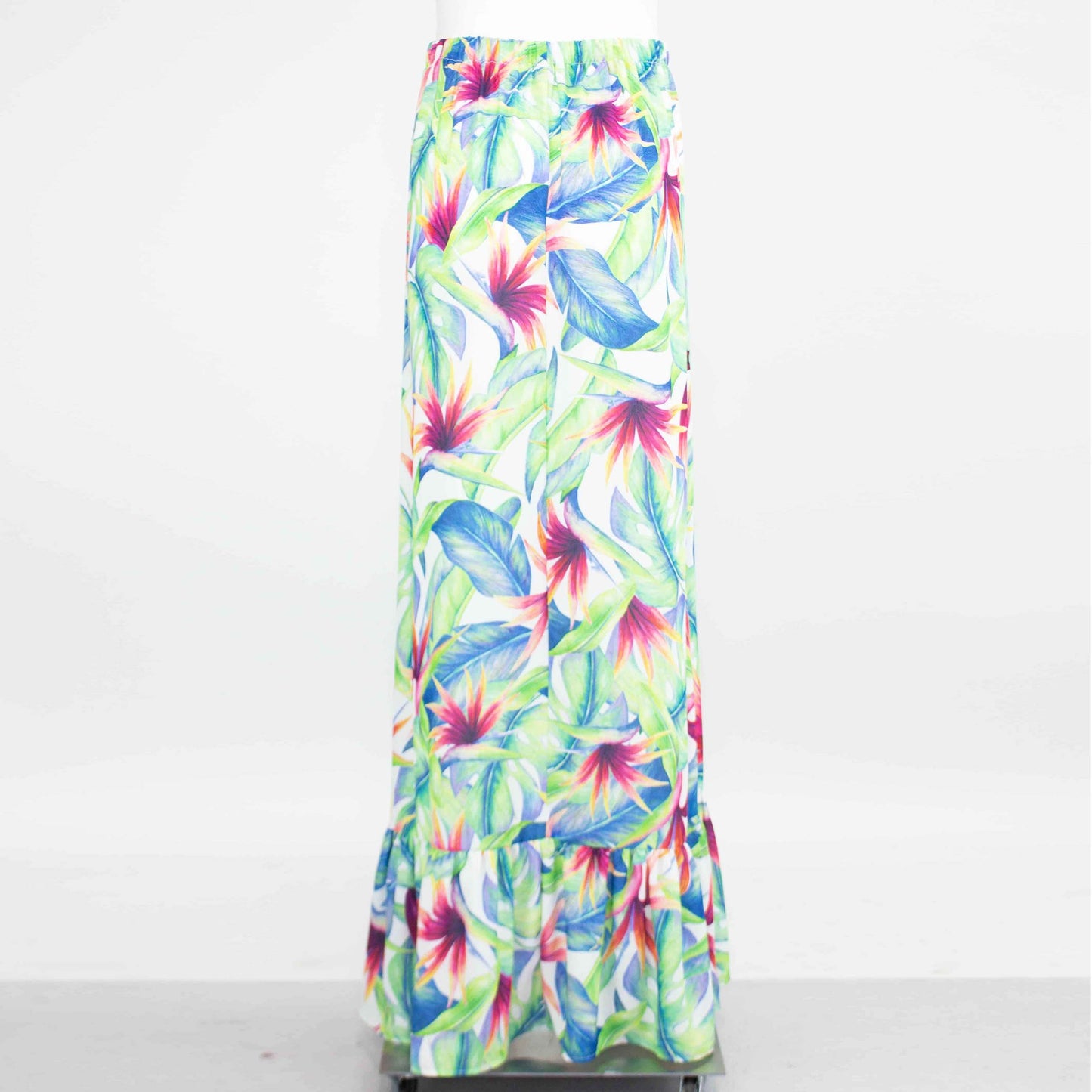 The Flared Bottom Tropical Maxi Skirt by Stylespect, showcasing large green leaves and bright pink flowers, is displayed on a mannequin against a white background.