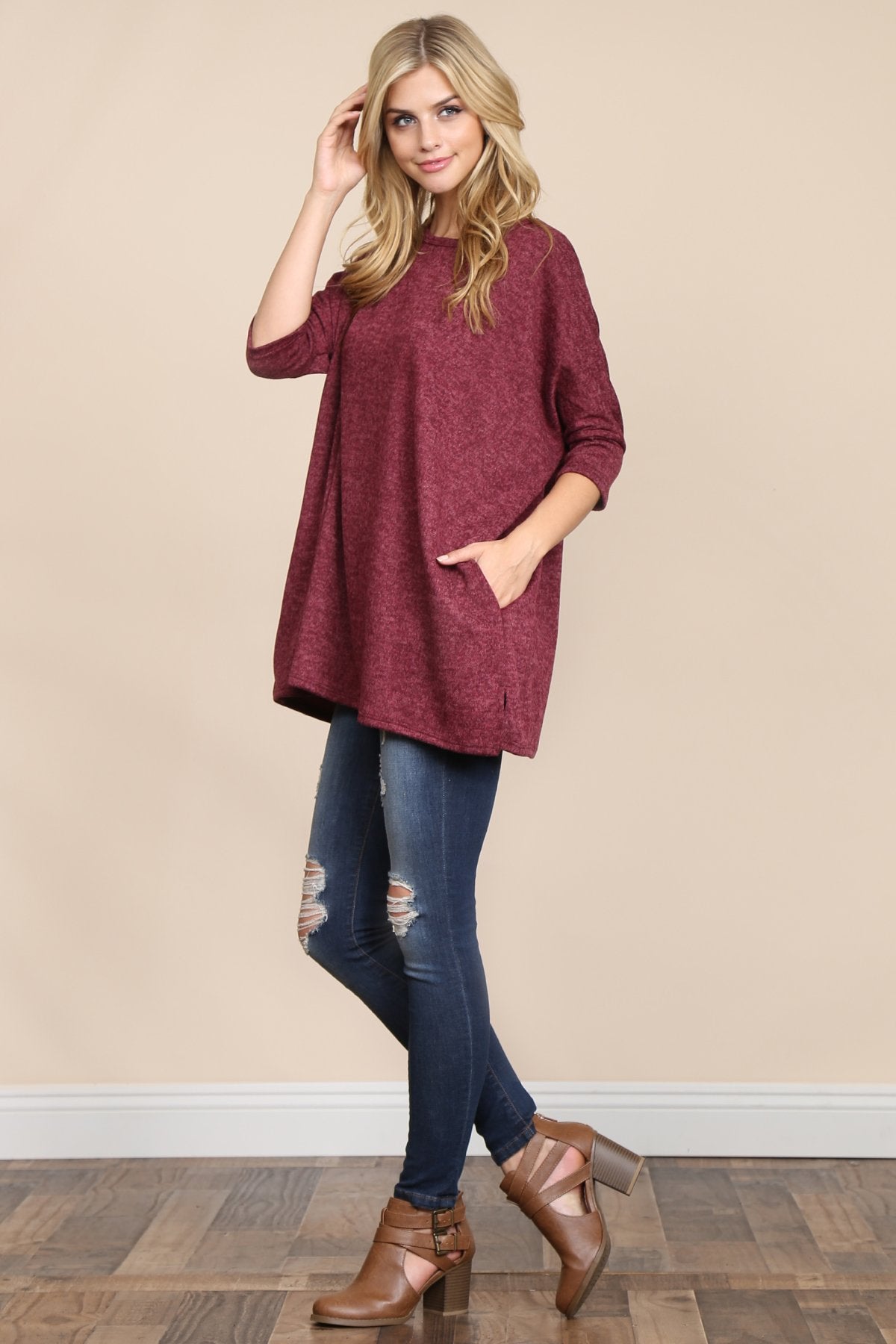 A woman stands against a beige background, wearing Riah Fashions Two Tone Hacci Oversized Dropped Shoulder Pocket Tunic in mustard, with hands in pockets and paired with ripped jeans.