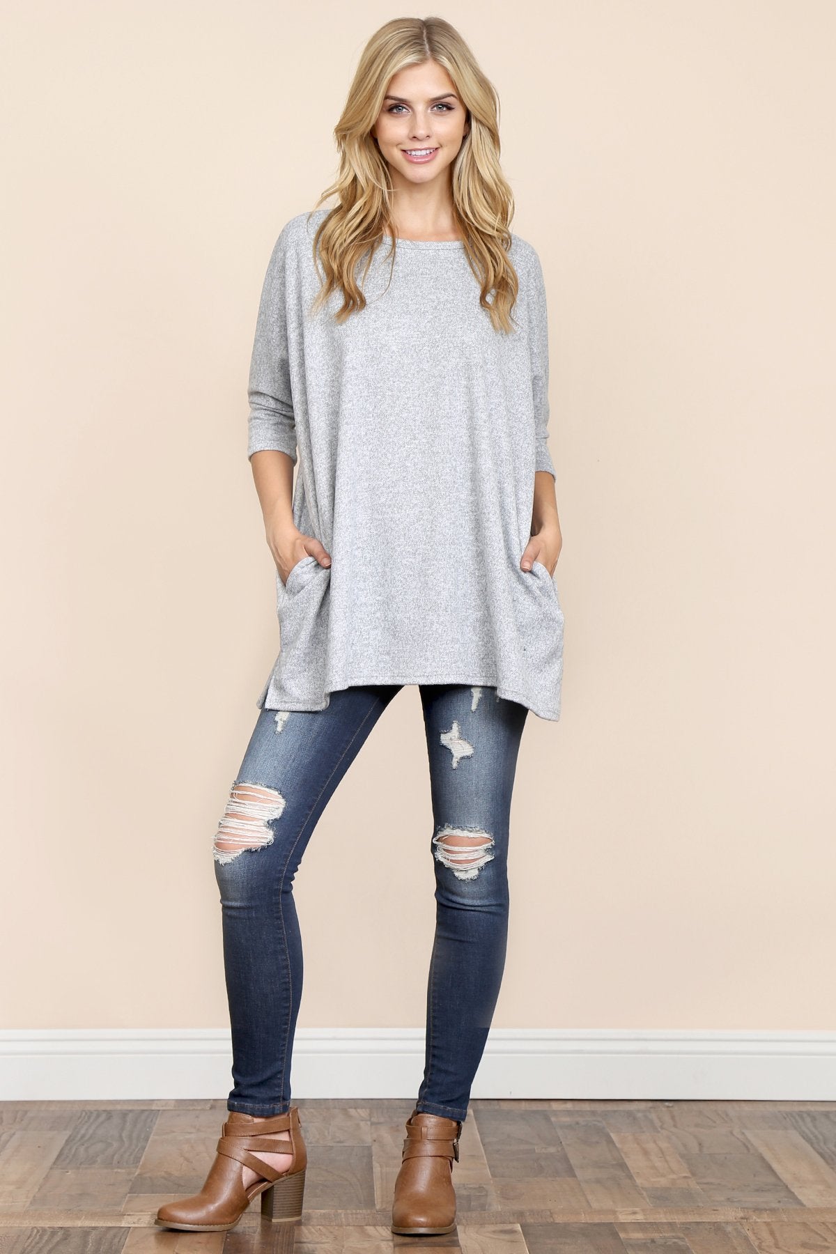 A woman stands against a beige background, wearing Riah Fashions Two Tone Hacci Oversized Dropped Shoulder Pocket Tunic in mustard, with hands in pockets and paired with ripped jeans.