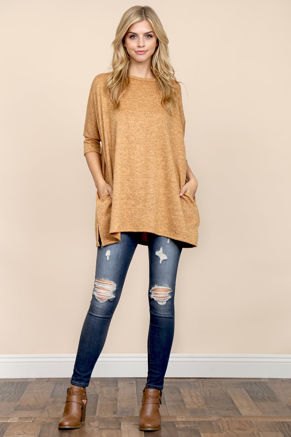 A woman stands against a beige background, wearing Riah Fashions Two Tone Hacci Oversized Dropped Shoulder Pocket Tunic in mustard, with hands in pockets and paired with ripped jeans.
