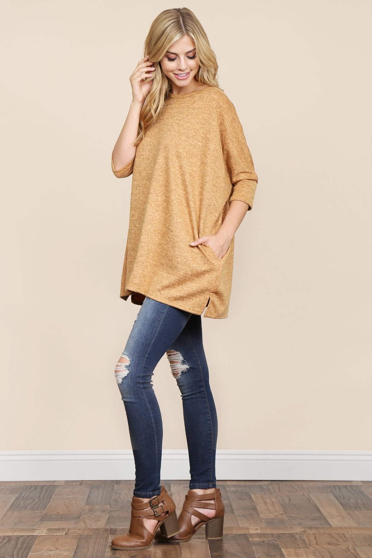A woman stands against a beige background, wearing Riah Fashions Two Tone Hacci Oversized Dropped Shoulder Pocket Tunic in mustard, with hands in pockets and paired with ripped jeans.