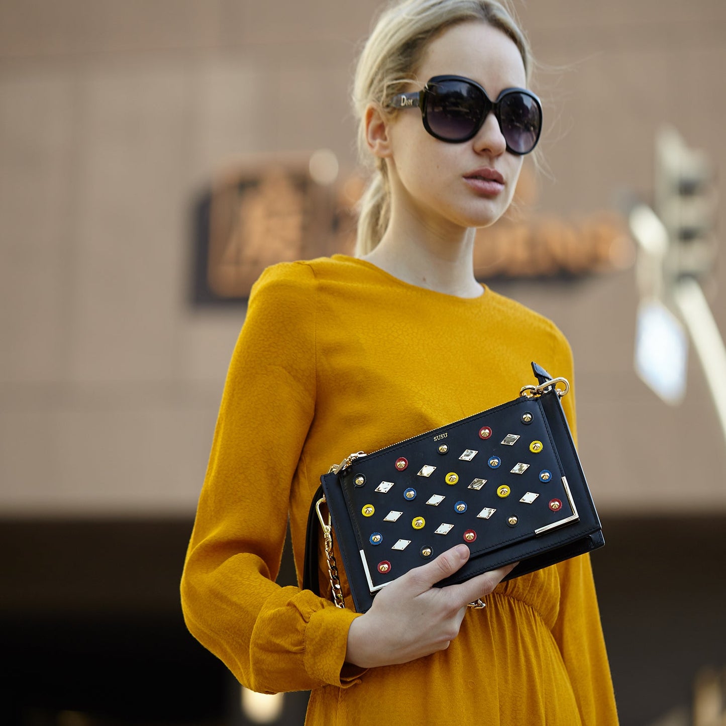 The SUSU Black Studded Crossbody Clutch boasts a design with colored studs, a gold chain, and gold diamond-shaped accents.