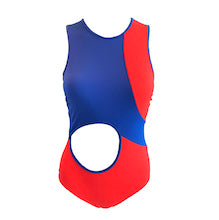 A woman in the Mirame Half Pipe swimsuit, featuring red and blue colors, shields her eyes from the sun while standing in front of a white tiled wall with a wavy pattern.