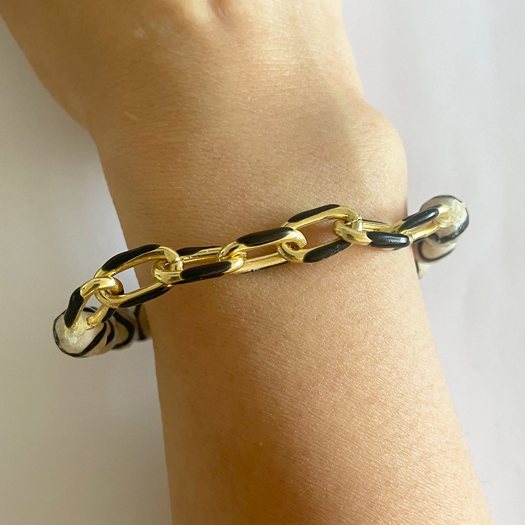 The Wavy Striped Agate Black Enamel Stretch Bracelet by Gena Myint features black and white striped beads with a gold and black chain clasp.