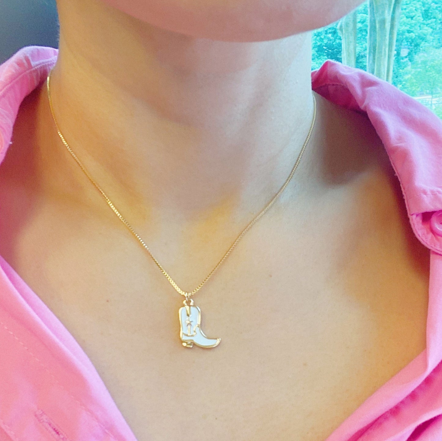 Two Cow Girl Boot Pendant Necklaces by Ellison + Young, one with a white boot and the other with a pink boot, are displayed on a marble surface.