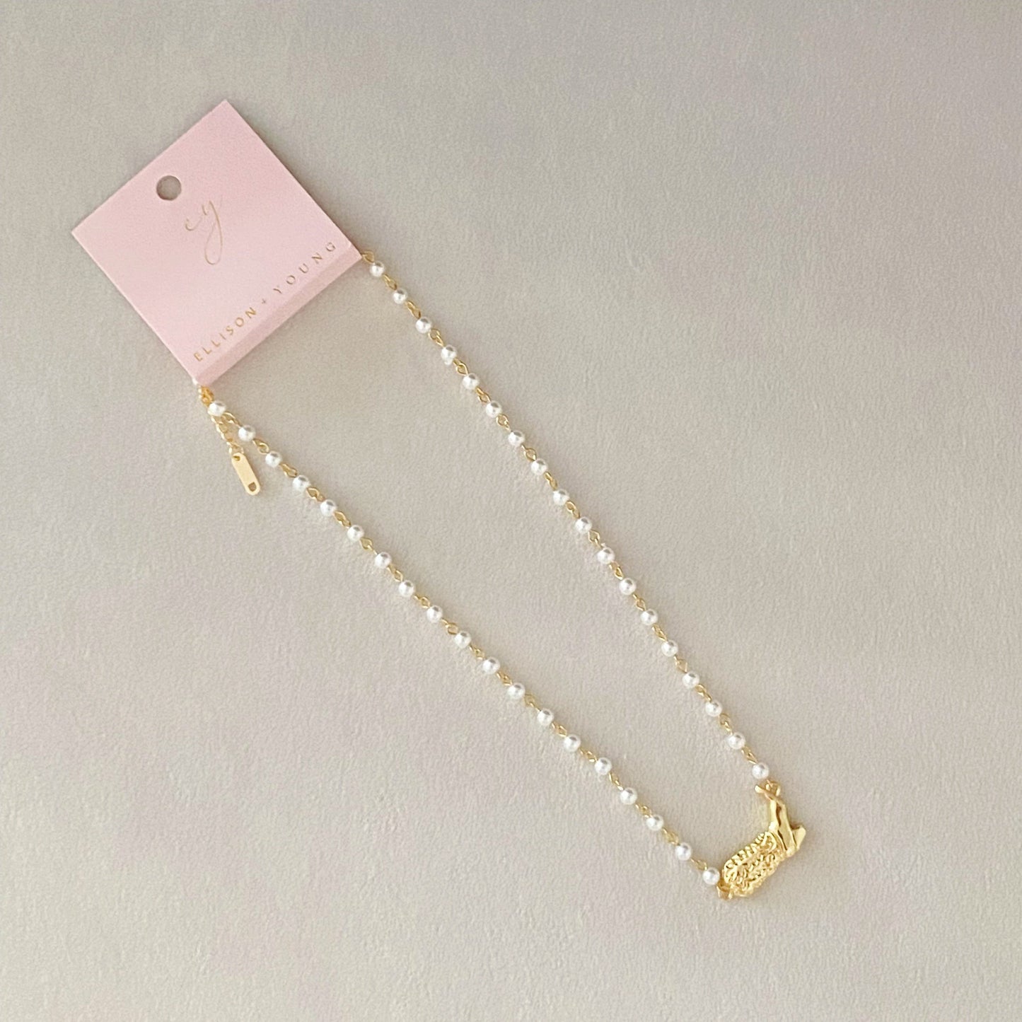 Ellison + Youngs Cowgirl Boot Pearl Chain Necklace is displayed on a marble surface.