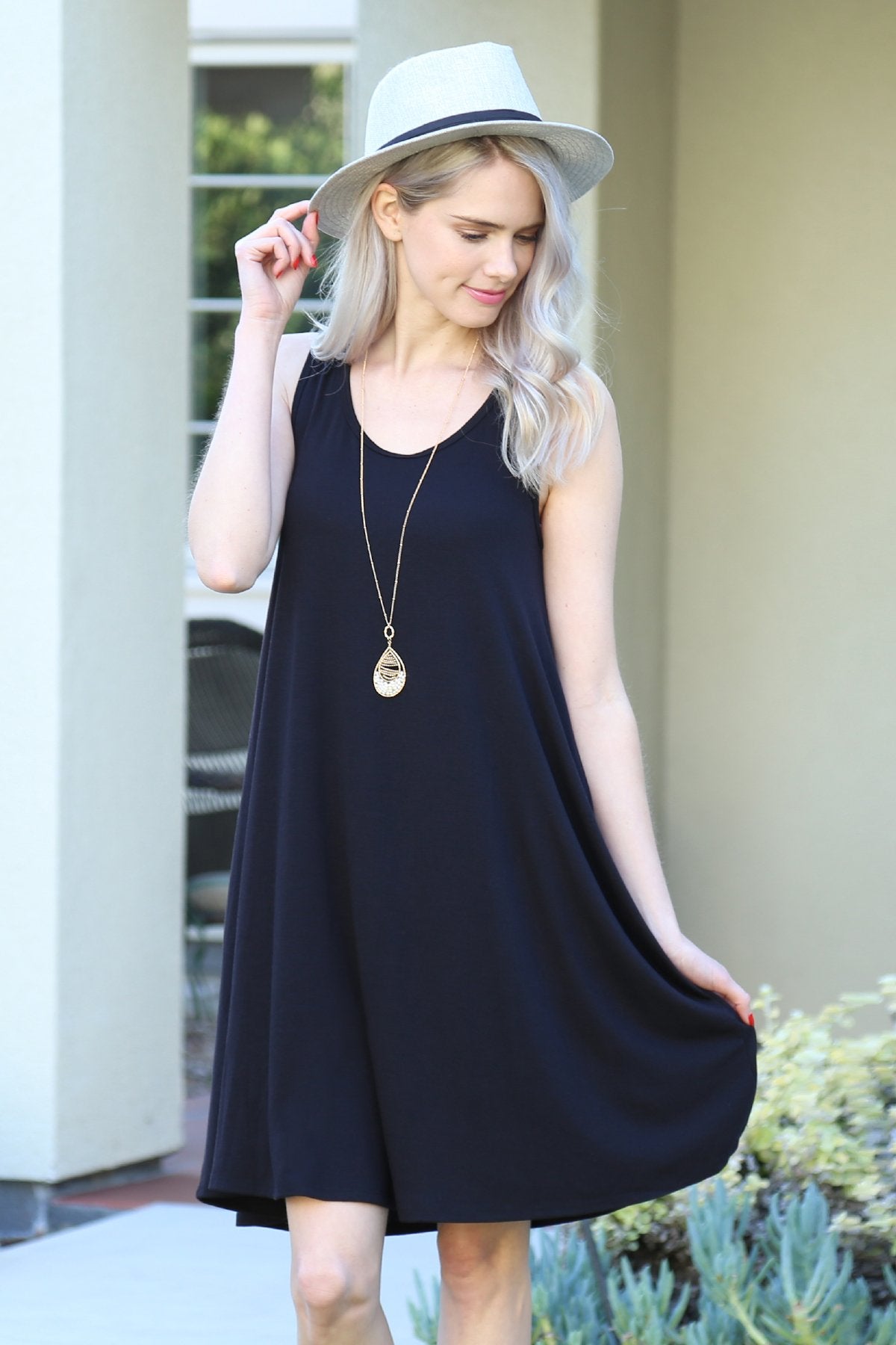 A person with long, light-colored hair wears a Sleeveless Flared Pocket Dress in light green by Riah Fashion outside, holding the dresss sides along with a triangular pendant necklace.