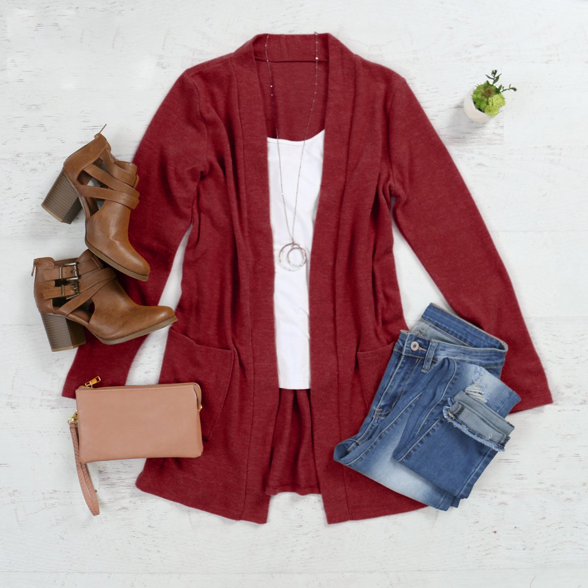 A woman in a Brushed Melange Open Front Cardigan by Riah Fashion and ripped jeans stands against a pink background, hands in her pockets.