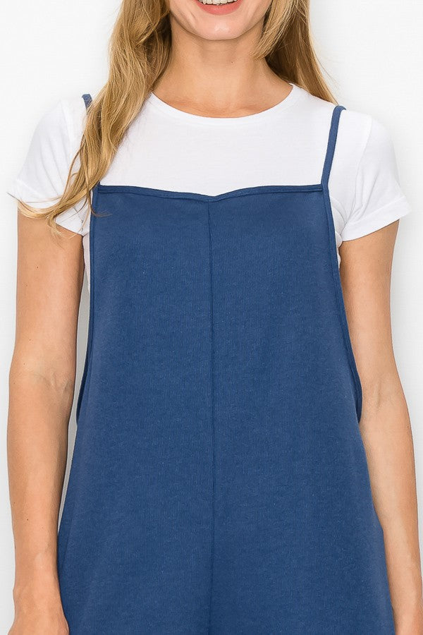 A person wearing a Stylespect Cropped Bottom Wide Leg Oversized Jumpsuit in blue over a white T-shirt and white sneakers, standing and smiling against a plain white background.