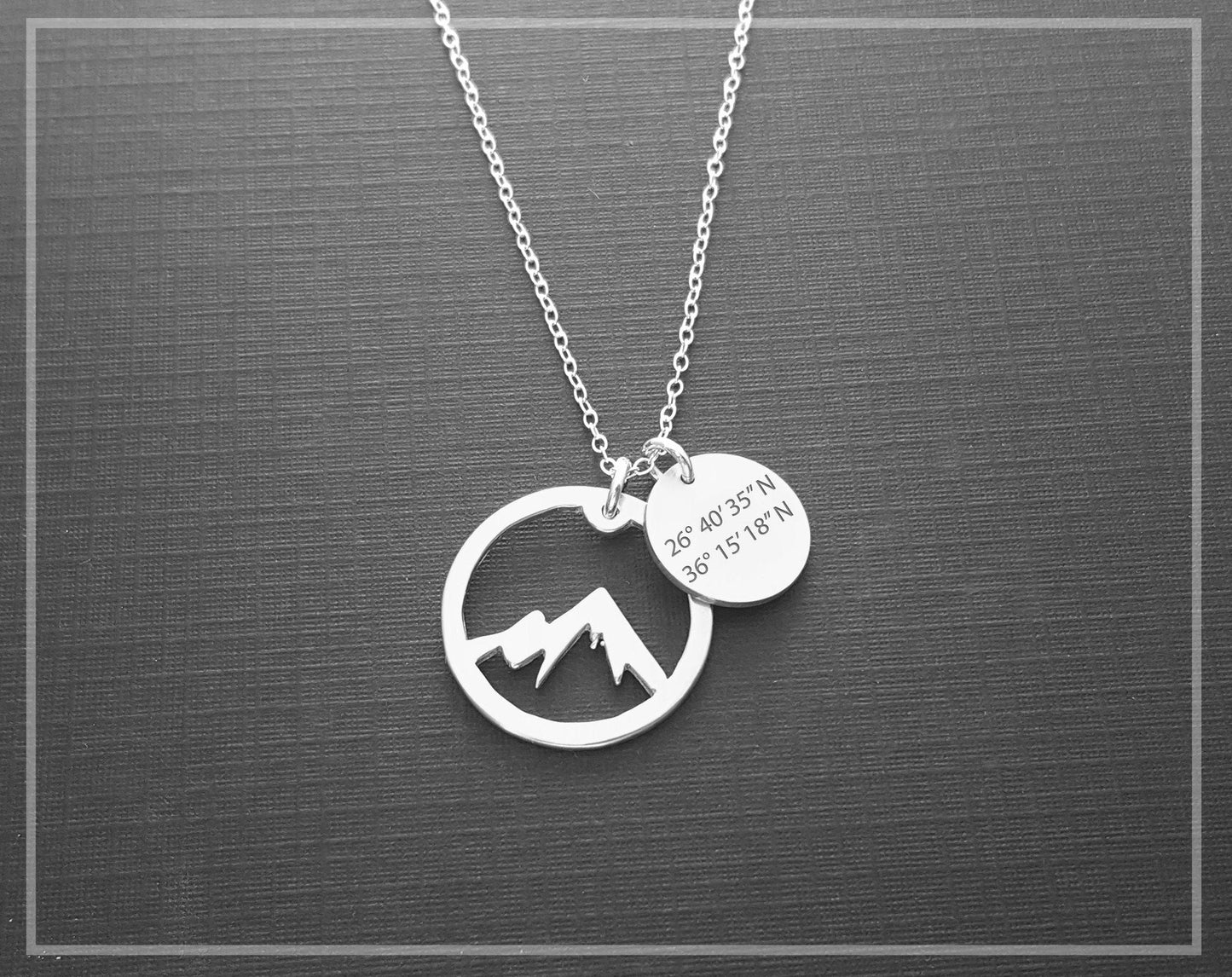 The Coordinate Mountain Necklace by Sincerely Silver is a silver piece featuring a mountain design pendant and a round one engraved with coordinates.