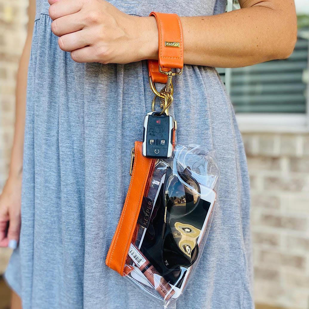 The KEYPER Persimmon Vegan Leather 2-Piece Wristlet Set features a clutch bag with a gold zipper, detachable strap, and small gold keychain.