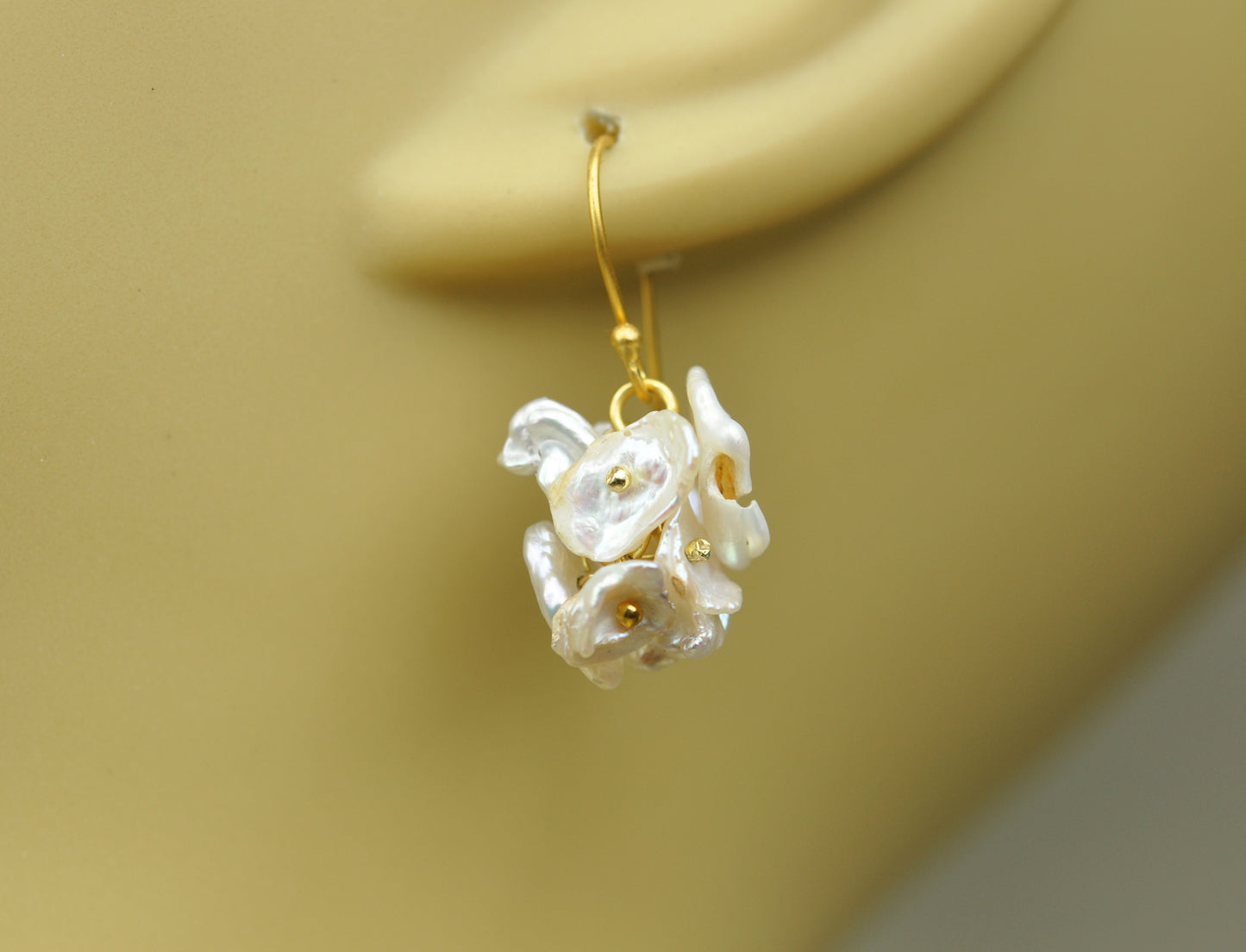 Gena Myints Short Keshi Pearl Cluster Earrings feature gold-hook dangling earrings adorned with clusters of petal-like motifs and gold bead accents.
