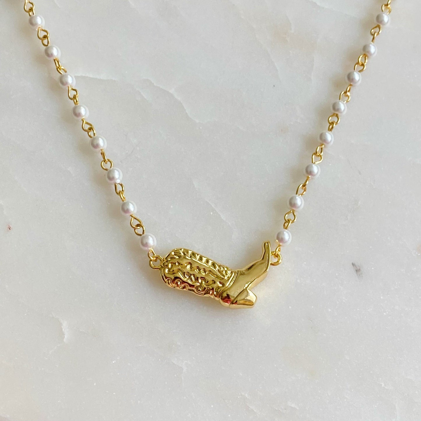 Ellison + Youngs Cowgirl Boot Pearl Chain Necklace is displayed on a marble surface.