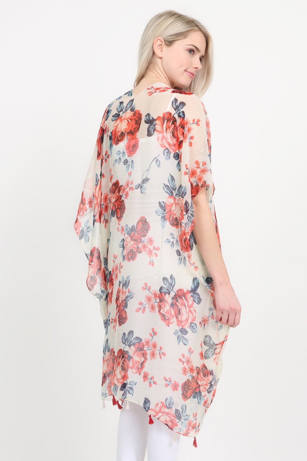 A woman stands against a plain background, wearing a Riah Fashion beige blue open front knee-length floral cardigan over a white outfit.