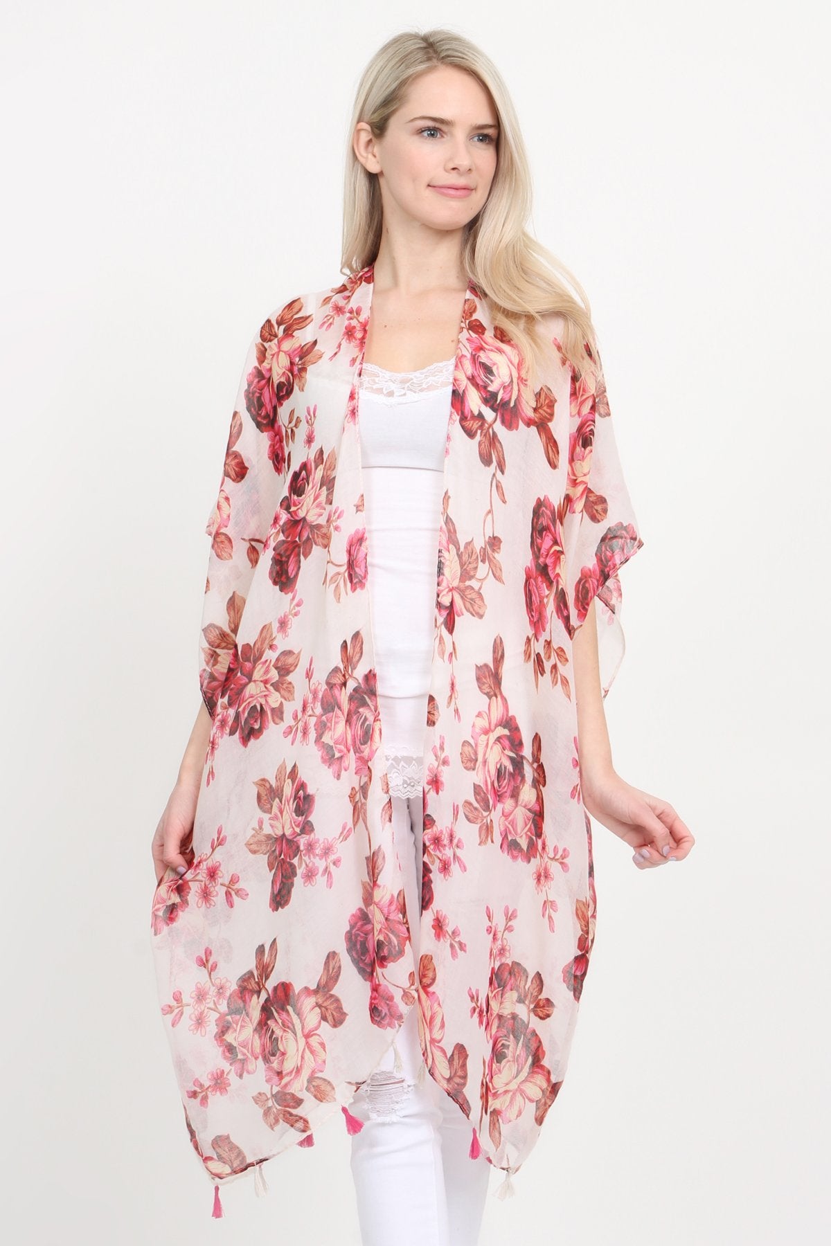 A woman stands against a plain background, wearing a Riah Fashion beige blue open front knee-length floral cardigan over a white outfit.