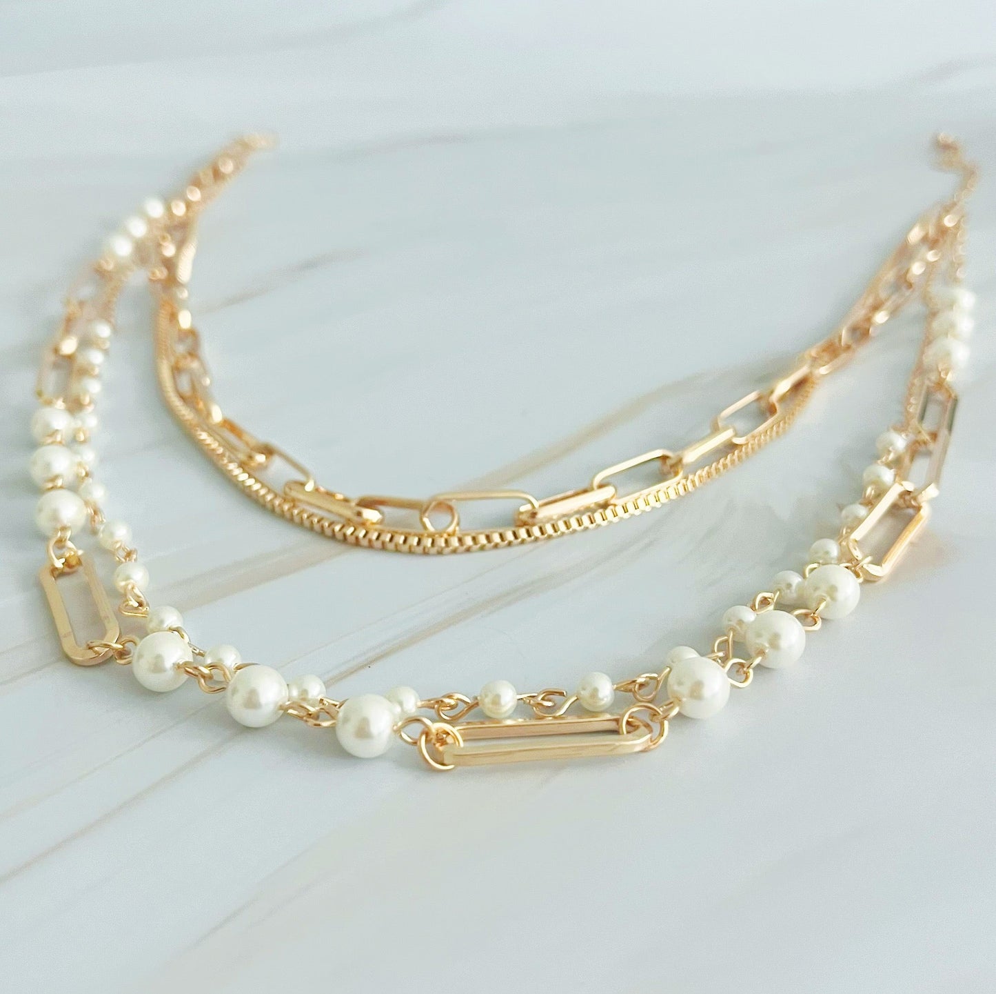 The Fourfect Layered Clip Chain Necklace by Ellison + Young displayed on a white marble surface.