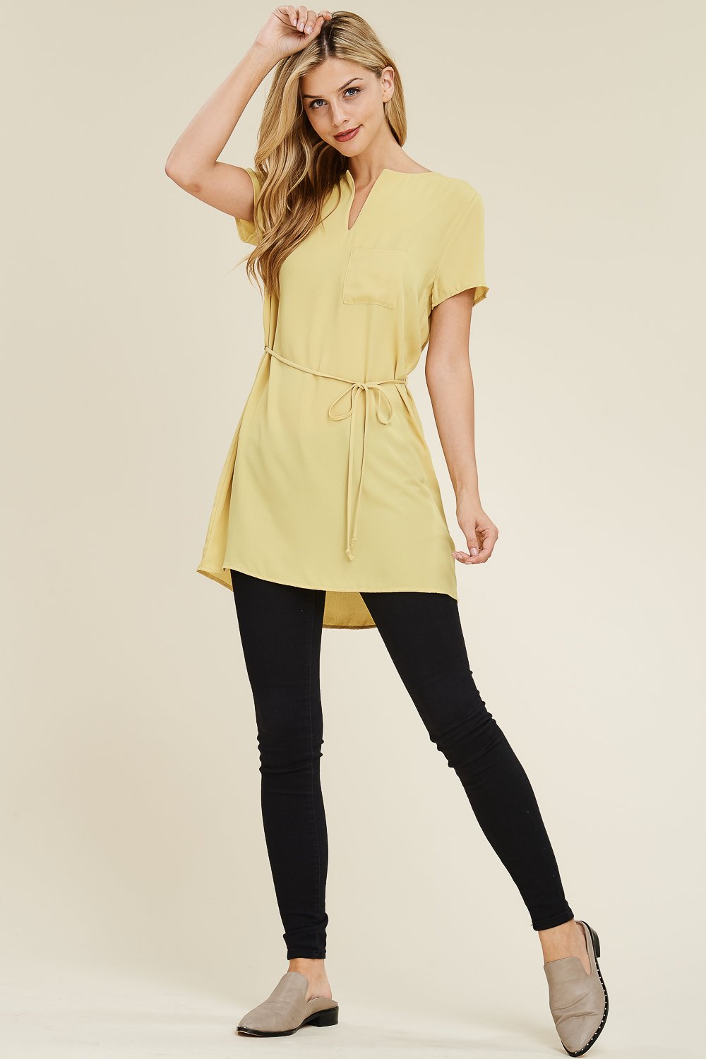 A woman wears a Riah Fashion Self Tie Waist Pocket Tunic Blouse, featuring a light yellow color with short sleeves, against a neutral background.