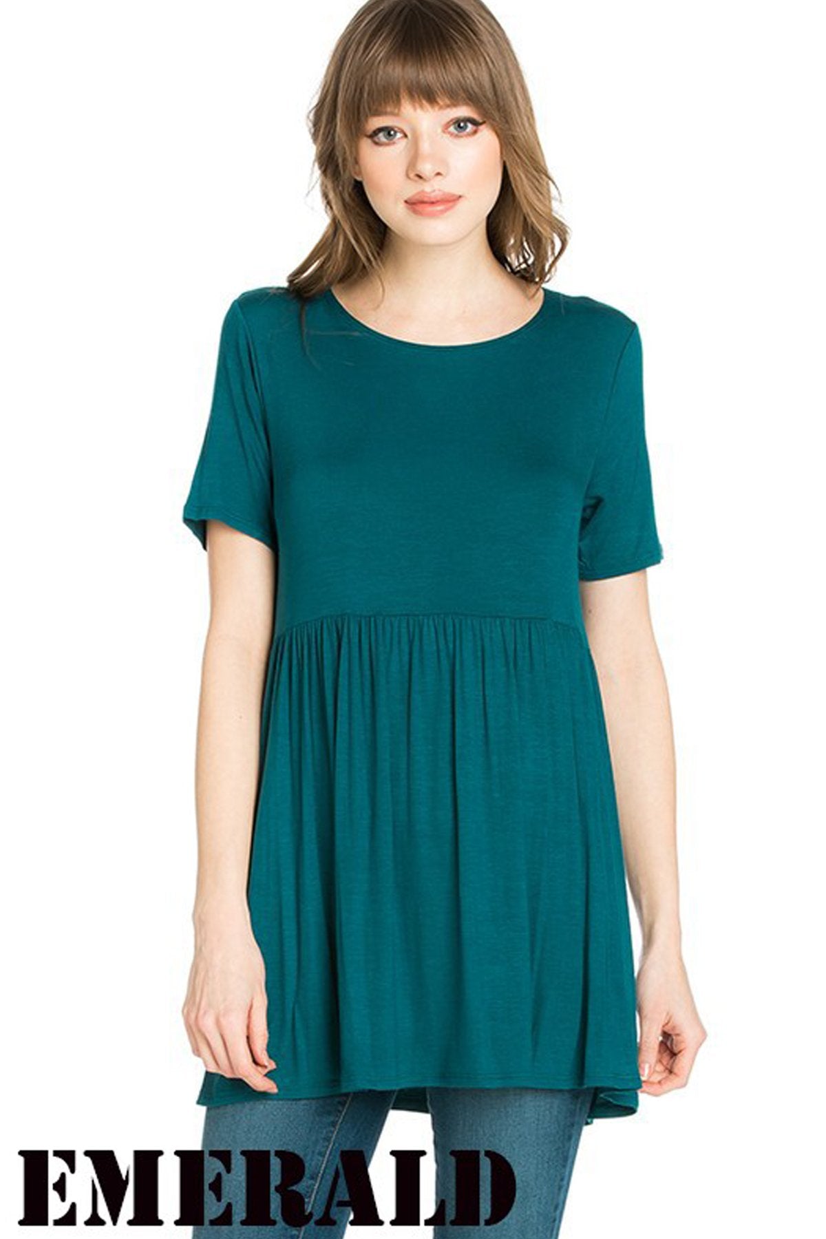 A woman stands outdoors wearing a beige Riah Fashion Short Sleeve Empire Waist Tunic paired with a long necklace.