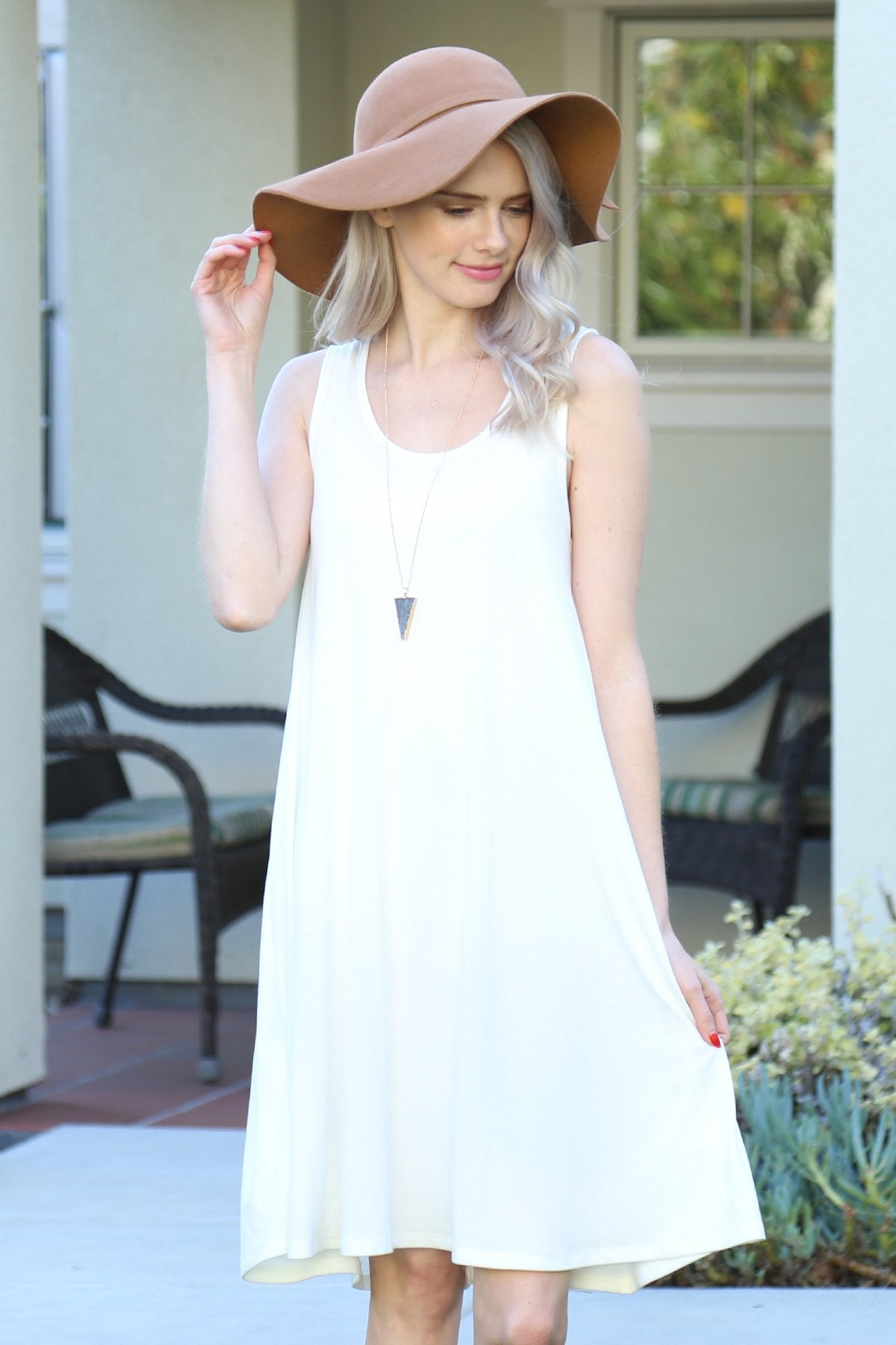 A person with long, light-colored hair wears a Sleeveless Flared Pocket Dress in light green by Riah Fashion outside, holding the dresss sides along with a triangular pendant necklace.
