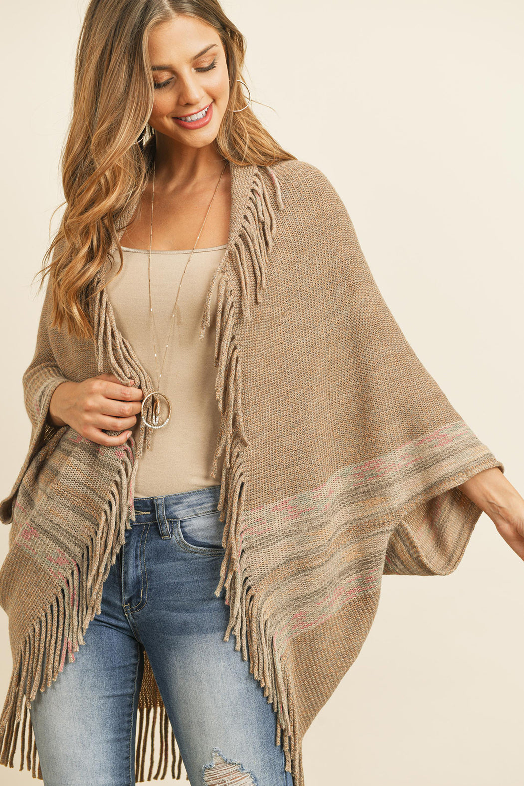 Someone is wearing a Fringe Stripe Open Front Kimono by Riah Fashion over a beige top and ripped jeans, standing against a plain background.