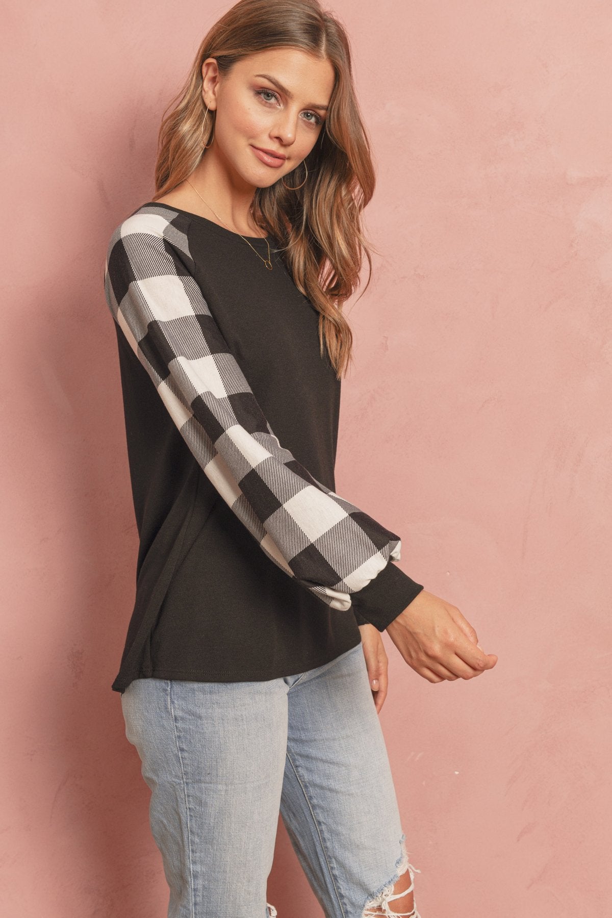 A woman wearing a faded denim plaid puff sleeved round neck top by Riah Fashion and ripped jeans stands against a plain background.