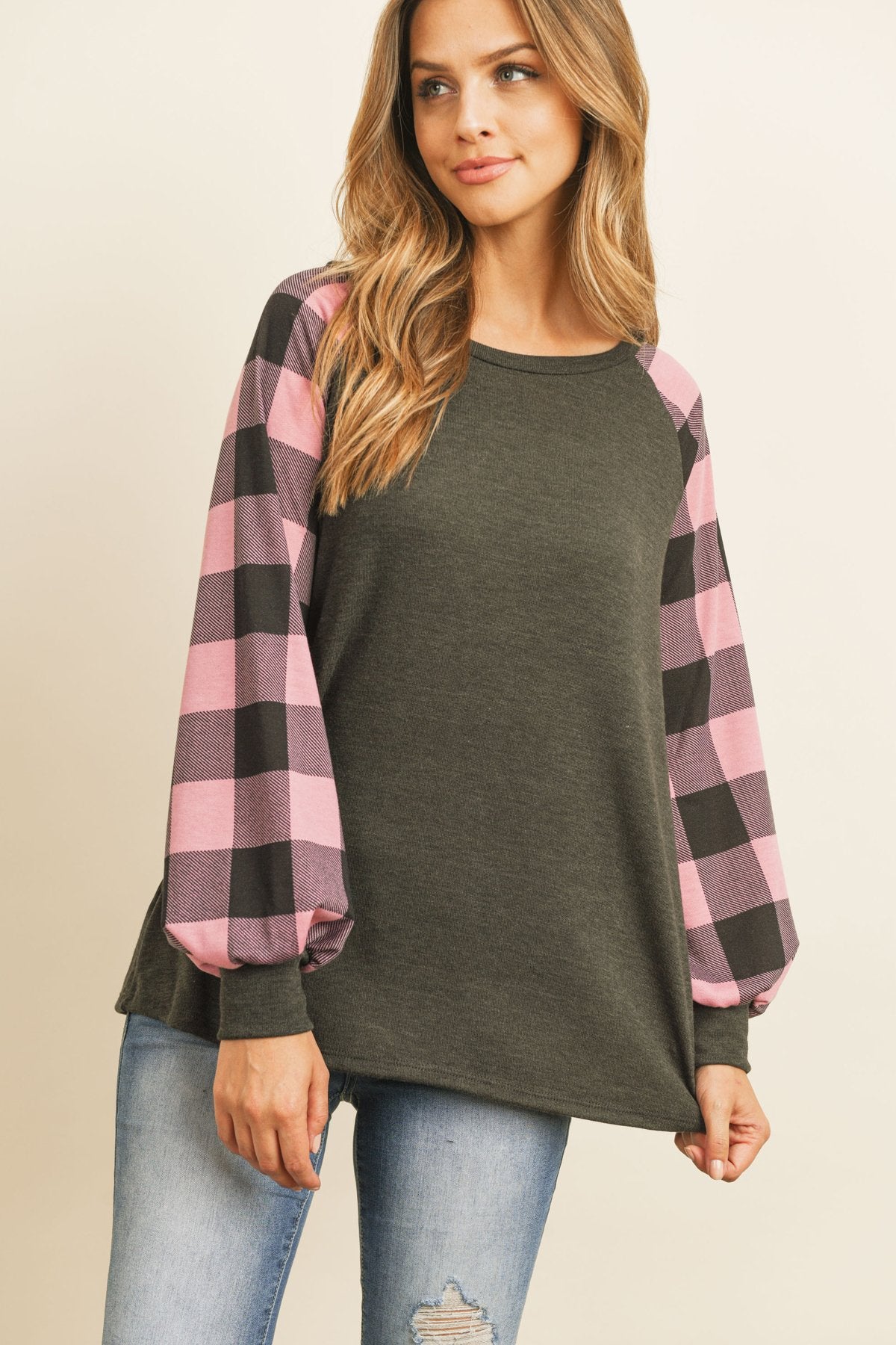 A woman wearing a faded denim plaid puff sleeved round neck top by Riah Fashion and ripped jeans stands against a plain background.