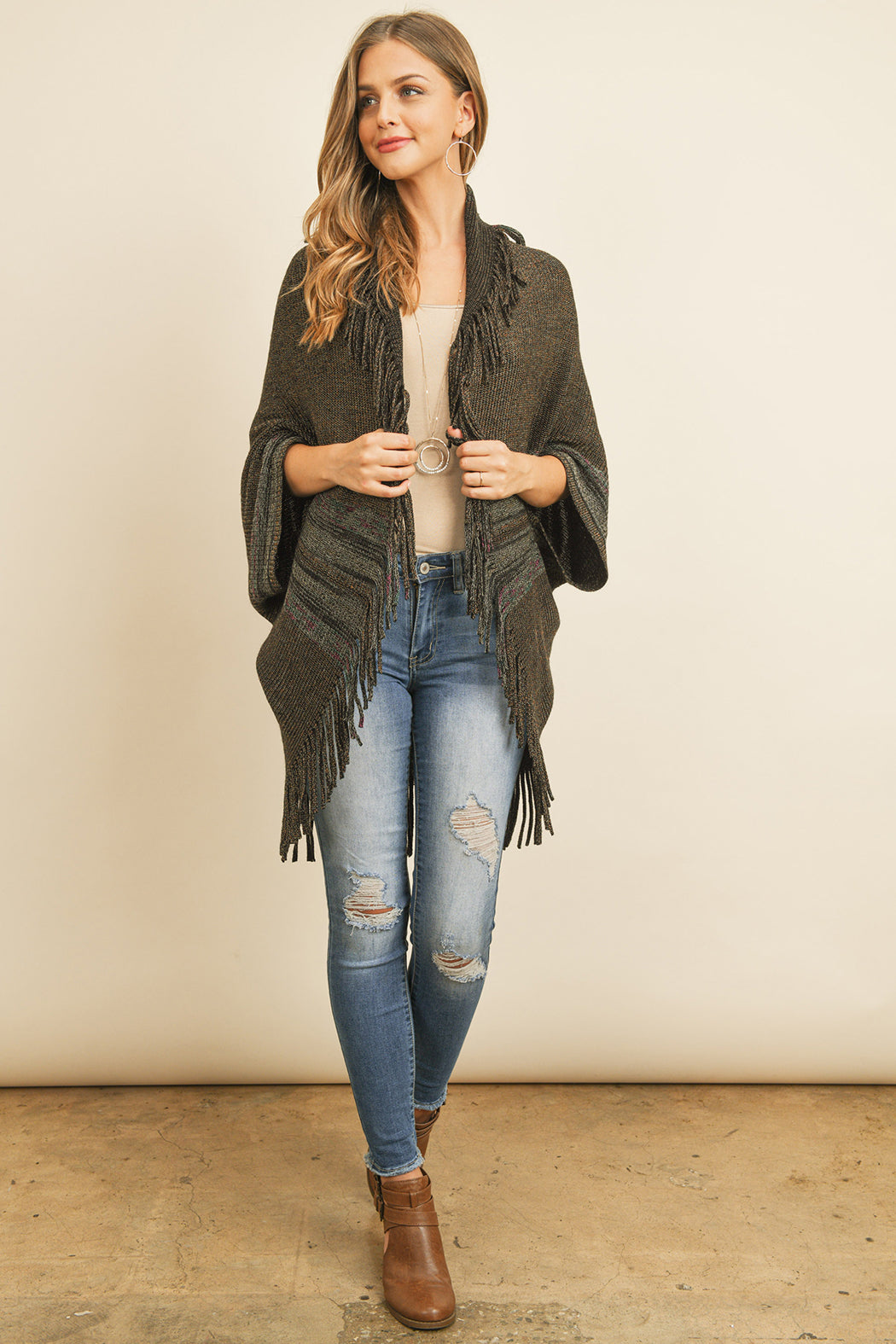 Someone is wearing a Fringe Stripe Open Front Kimono by Riah Fashion over a beige top and ripped jeans, standing against a plain background.