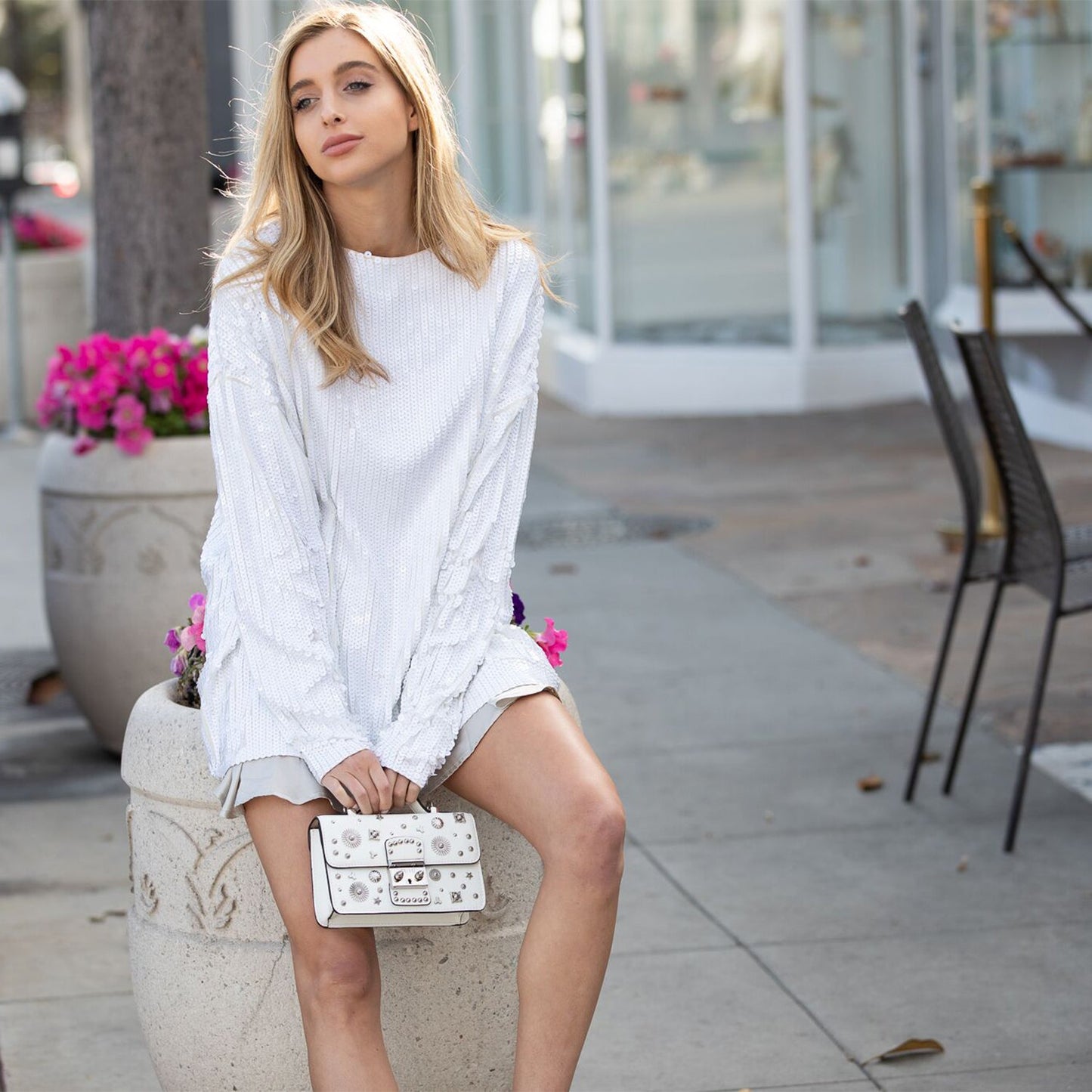 The Hollywood White Leather Crossbody Bag by SUSU features silver stud embellishments, a chain strap, a top handle, and a front clasp with the SUSU brand name.