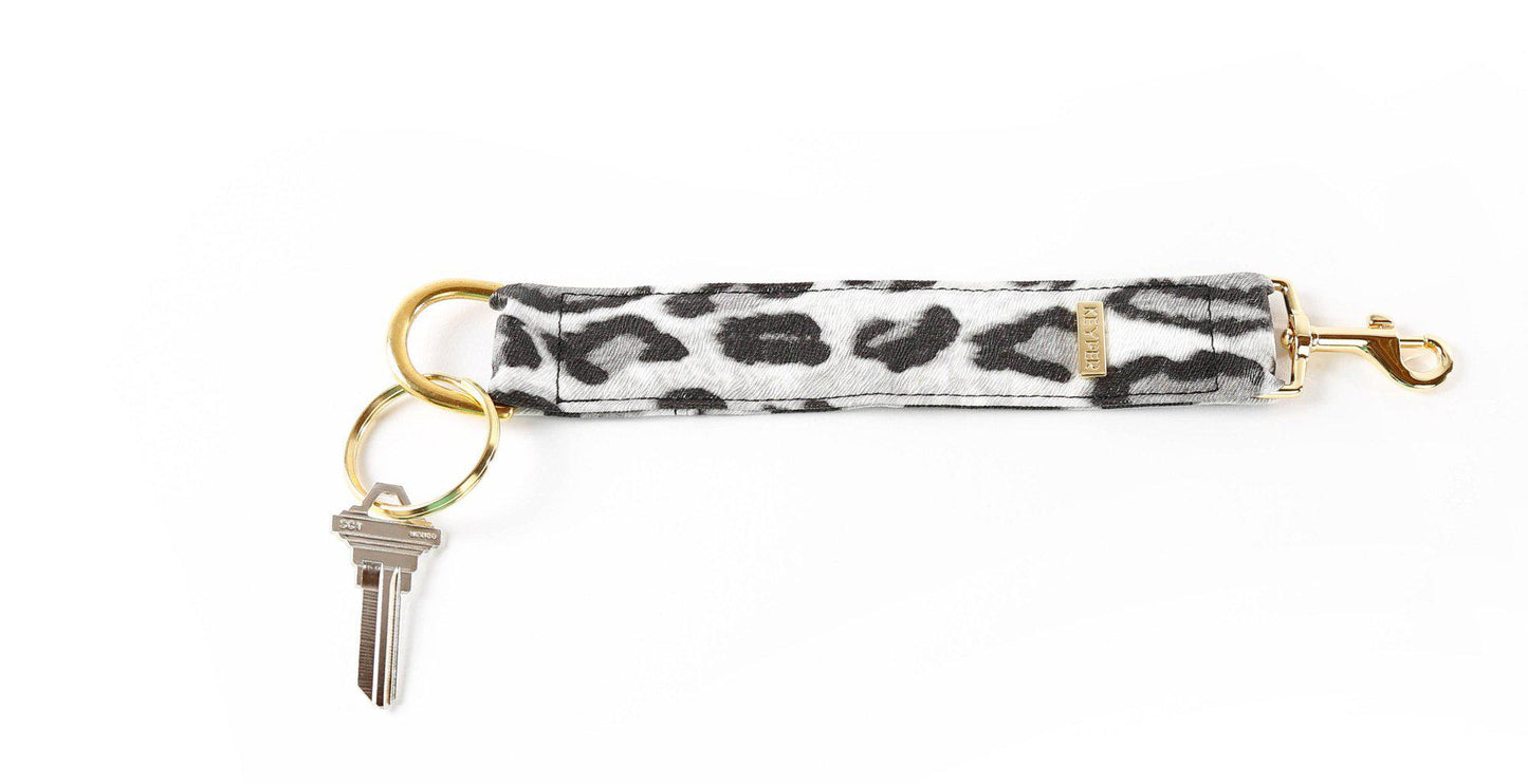 The KEYPER brands Snow Leopard Vegan Leather KEYPER® Key Ring features a leopard print design, a gold key ring with an attached key, and a small rectangular gold label.