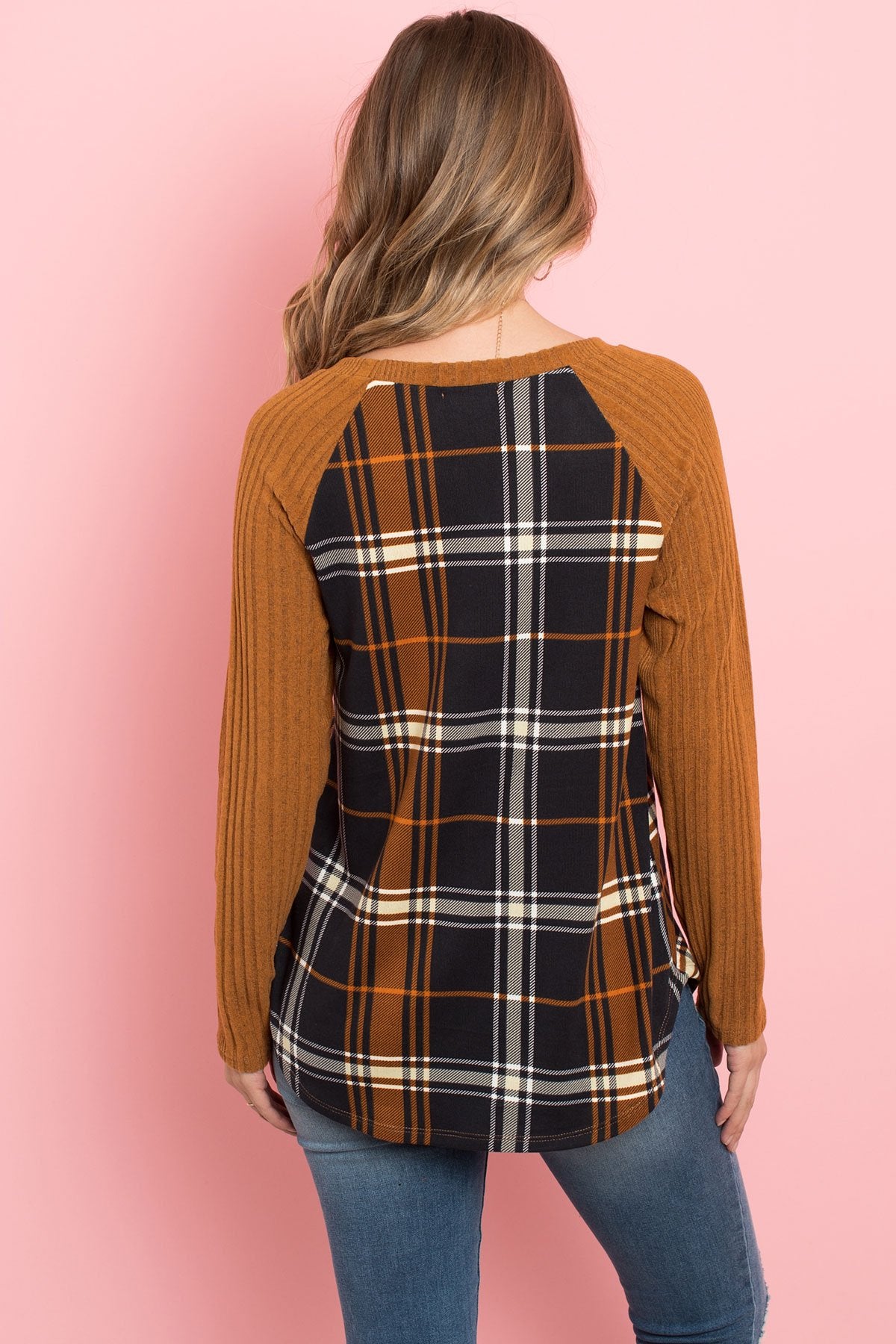 A person wearing a Riah Fashion Long Sleeve Knit Detail Contrast Plaid Top and jeans stands against a pink background, smiling.