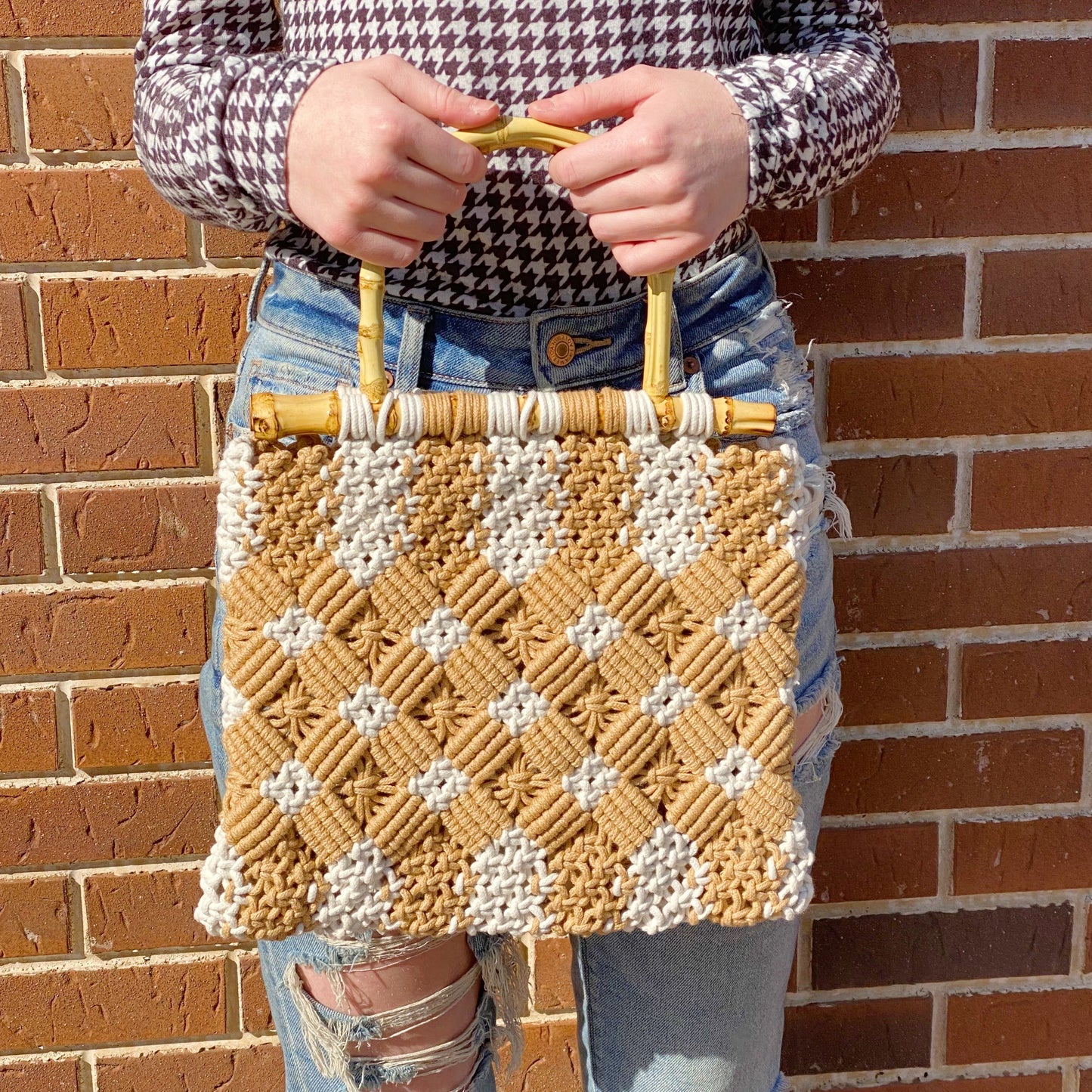A person holds the Ellison + Young Bamboo Babe Tote, wearing a houndstooth shirt and ripped jeans. The background features a paved walkway and street.