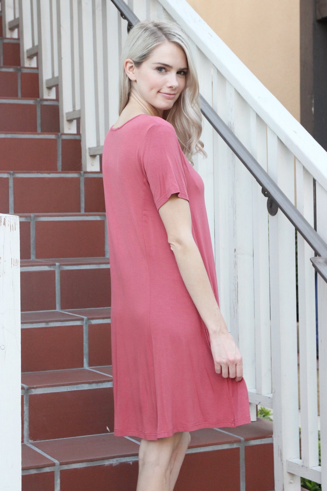 A person with long hair wearing a rust-colored Short Sleeve Strappy Pocket Dress by Riah Fashion stands on a staircase, holding the side of the dress with one hand.